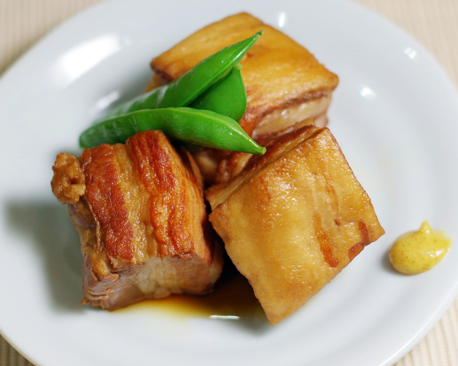Drei Stücke knuspriger Schweinebauch mit grünen Bohnen auf einem weißen Teller