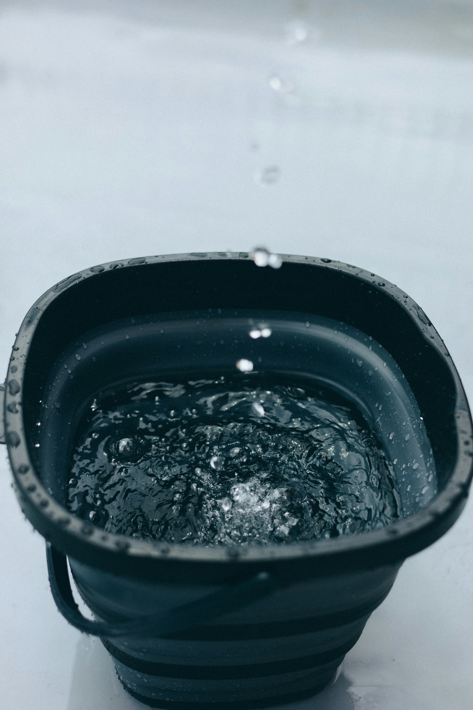 一個裝滿水的黑色桶，水滴正在掉入其中