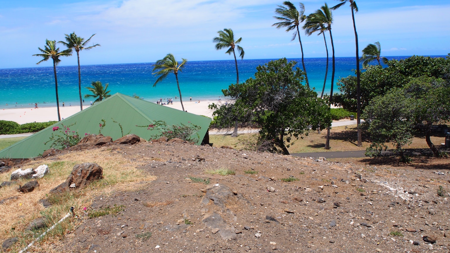 Scenic view of a beach with blue ocean and white sand green-roofed building and palm trees