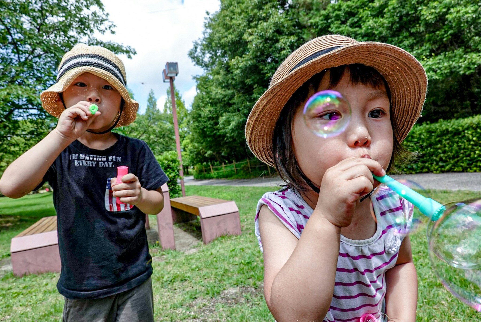 芝生の公園でストローのジュースを飲む帽子姿の子どもたち