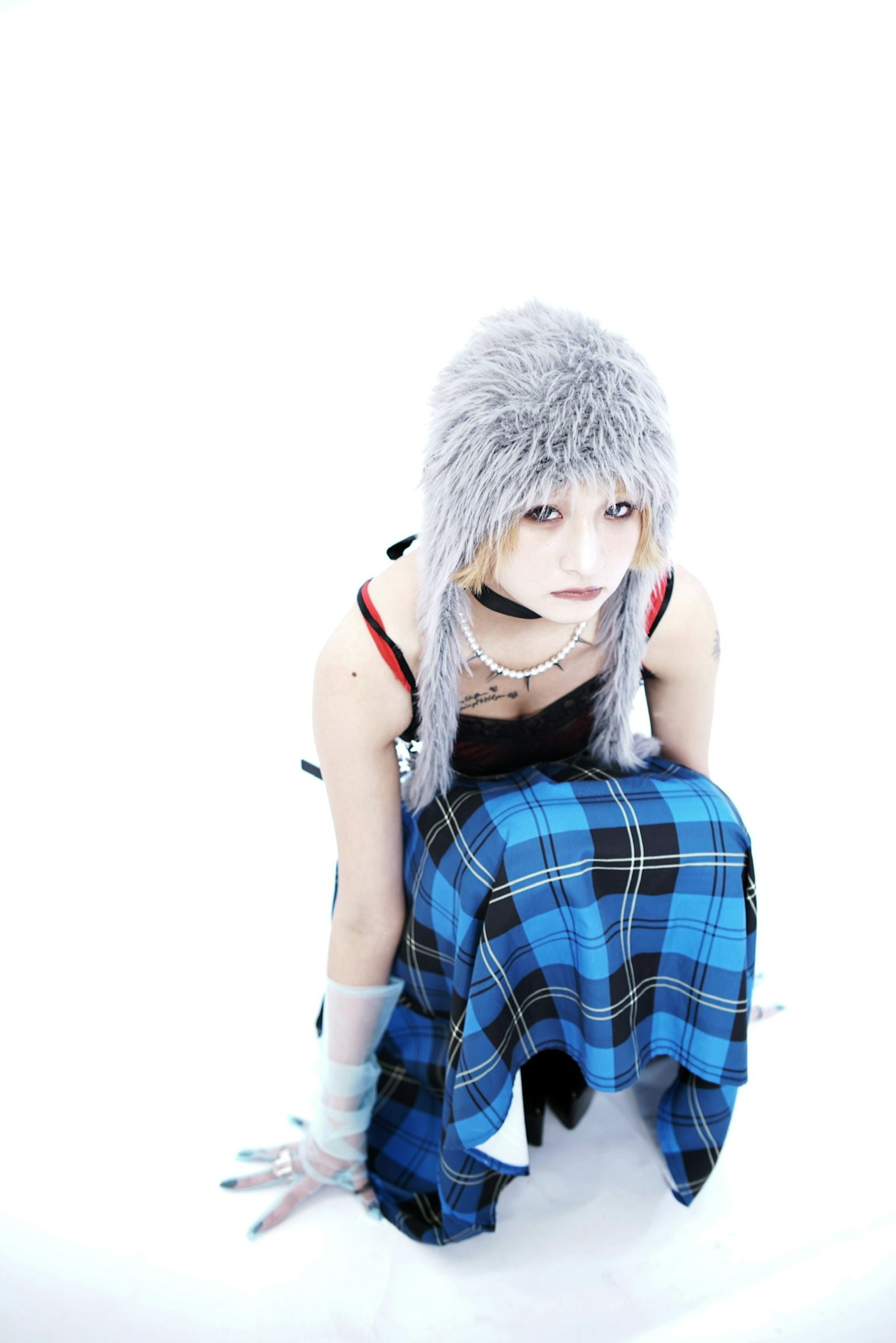 白い背景の前に座る銀髪の女性 コスチュームにチェック柄のスカートを着用