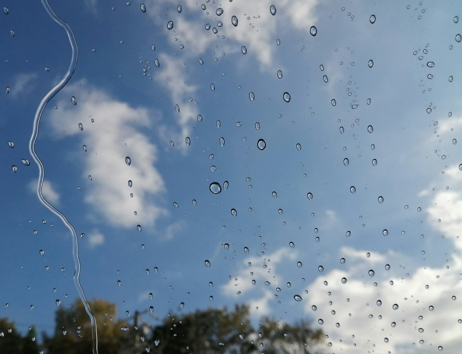 Gouttes de pluie sur une fenêtre avec ciel bleu et nuages blancs