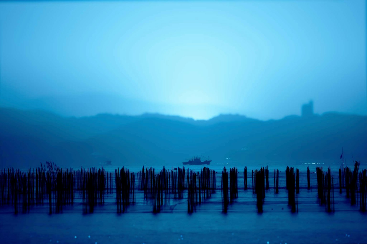 Misty blue ocean view with mountains in the background reflections on the water surface wooden posts