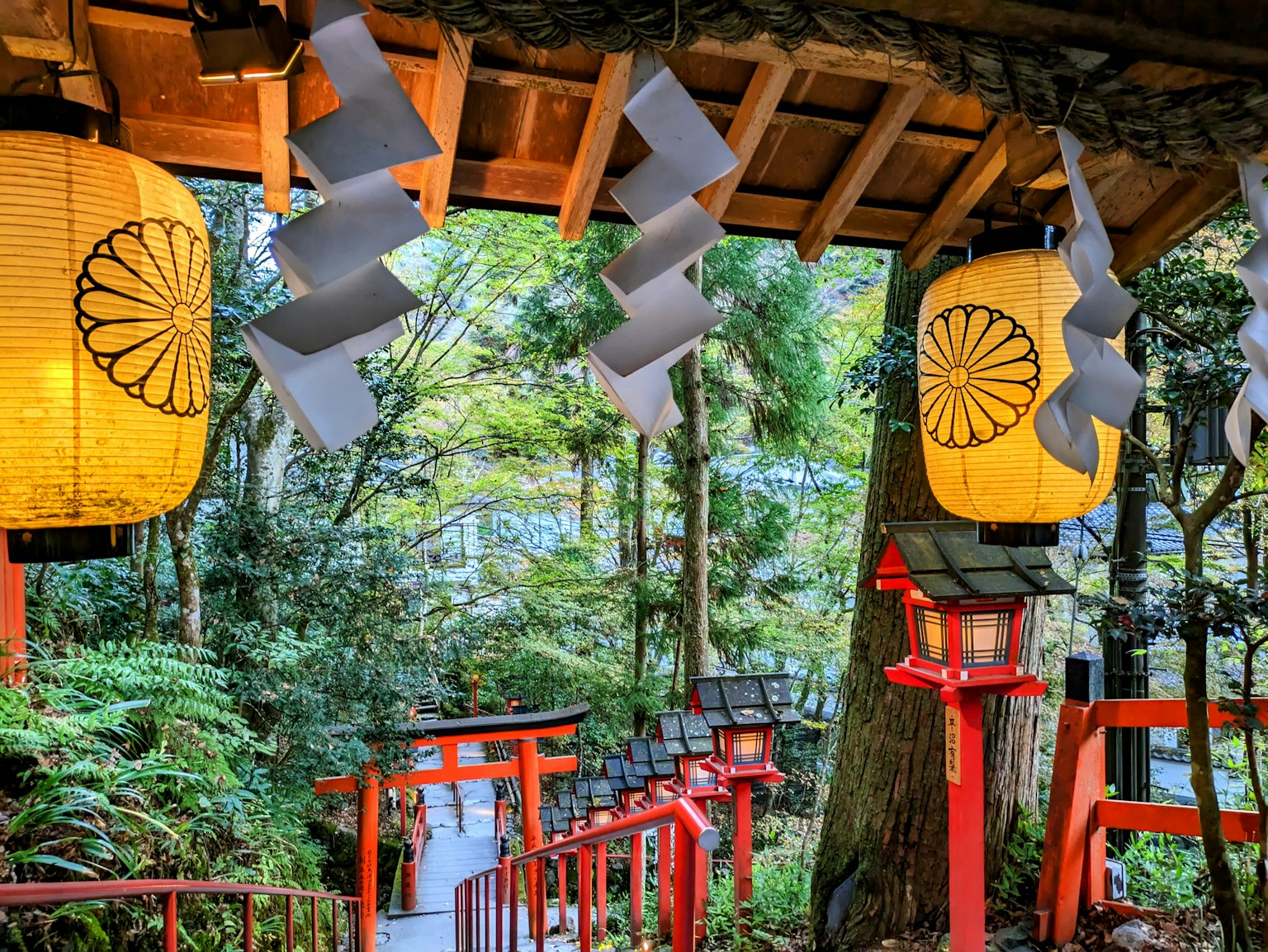 Ingresso di un santuario circondato da una vegetazione lussureggiante con lanterne e porte torii