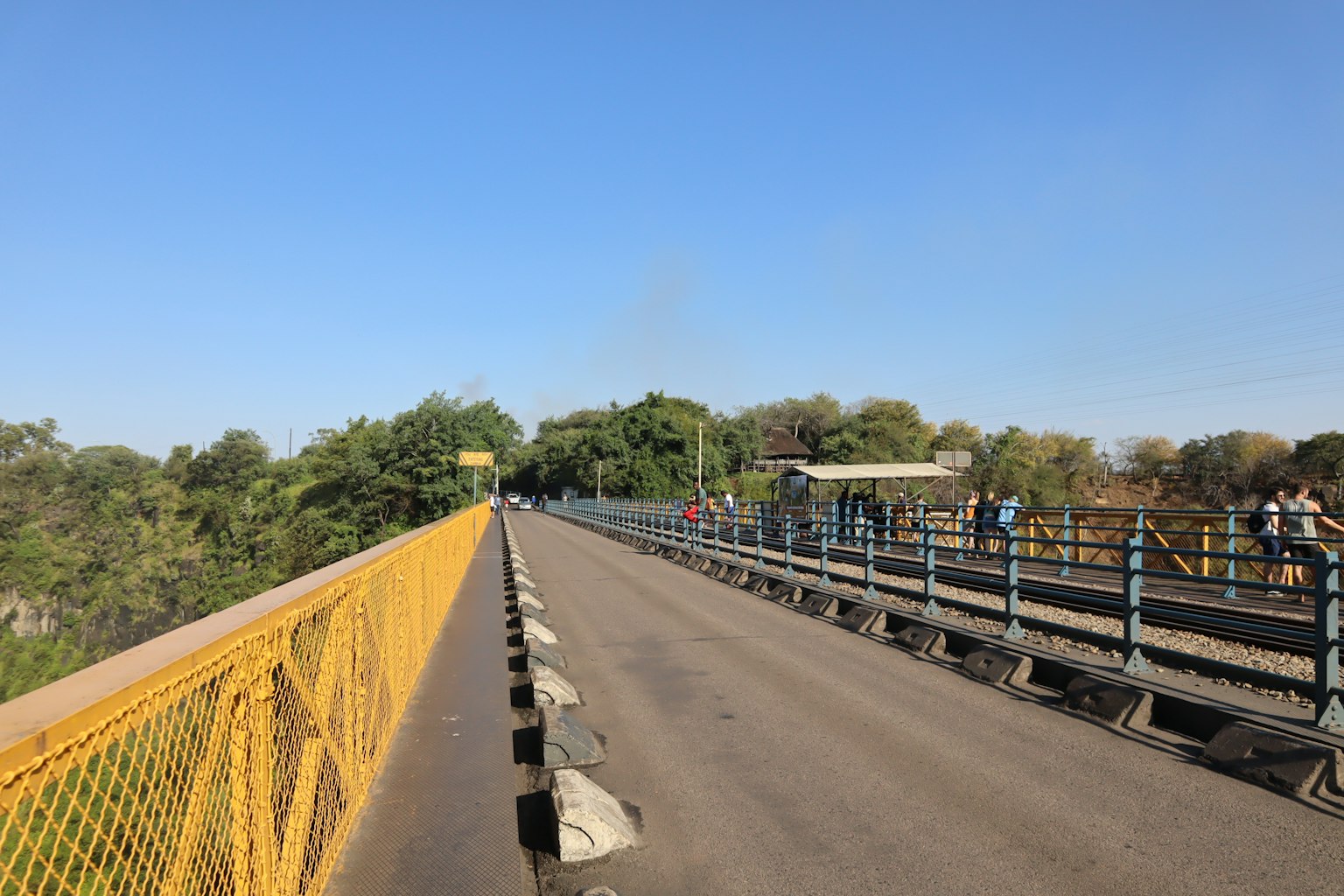 Paesaggio di un ponte con parapetto giallo circondato da alberi verdi e cielo blu