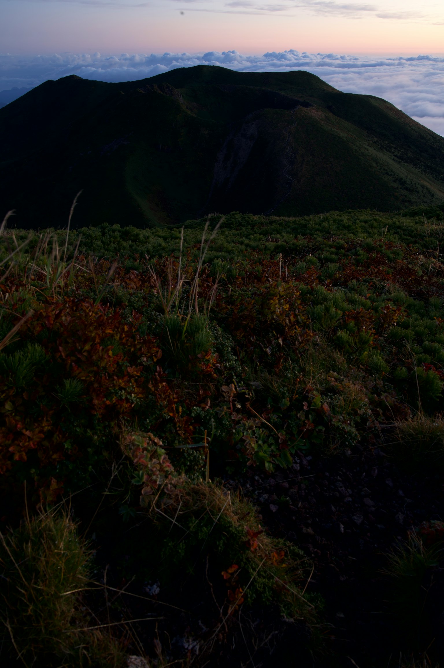 Sonnenuntergangsblick vom Berggipfel mit grünem Vordergrund und entfernten Hügeln