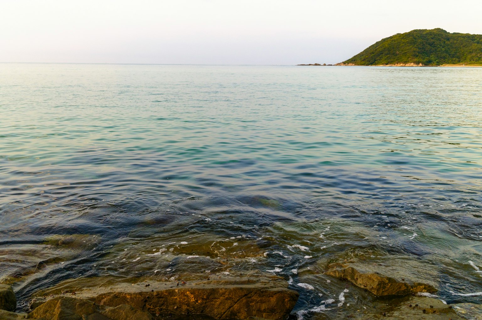 Mar tranquilo con rocas y colina a lo lejos