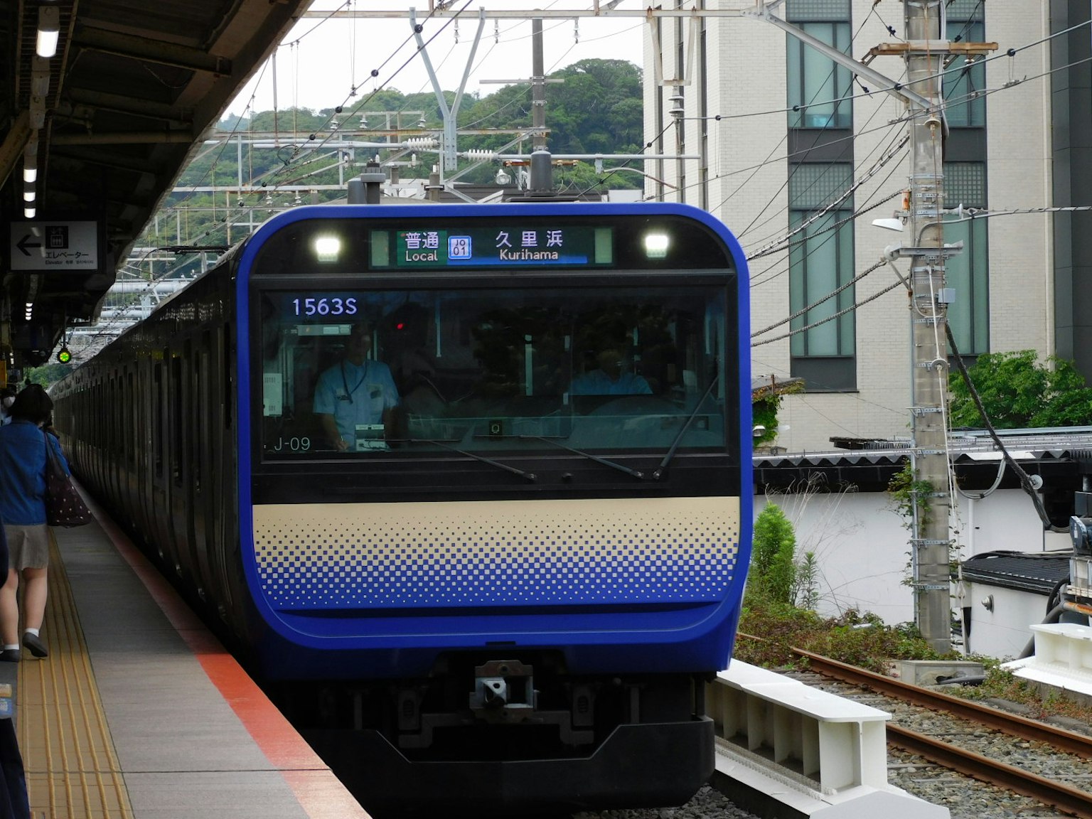 Kereta biru berhenti di stasiun dengan bangunan di sekitarnya