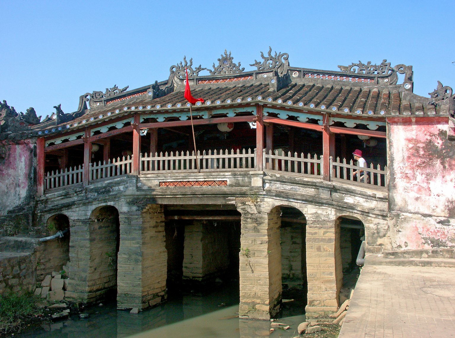 Architettura tradizionale di un ponte vietnamita con bandiera rossa che attraversa un fiume