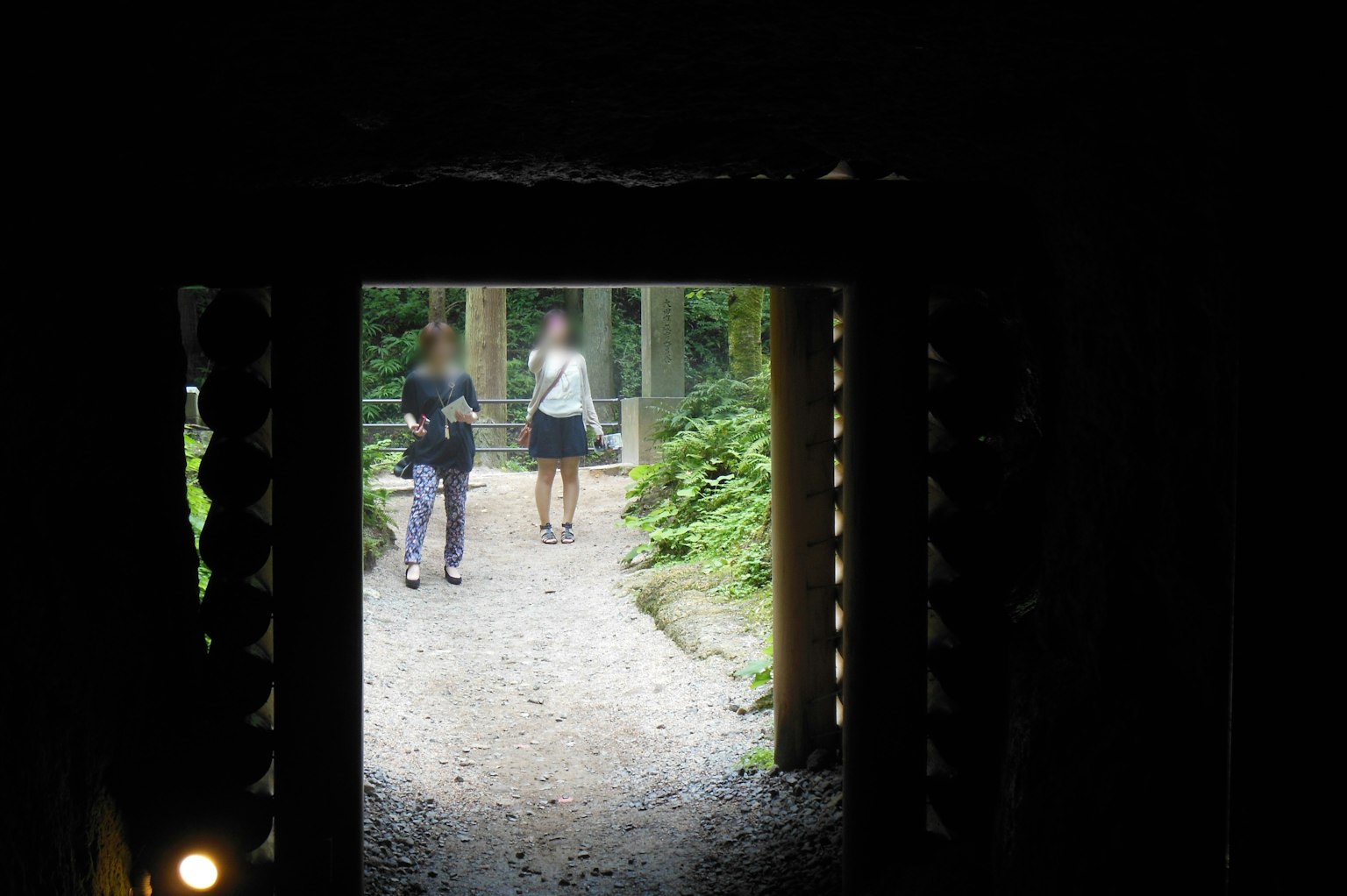 Vista a través de un túnel oscuro hacia un paisaje verde con dos mujeres