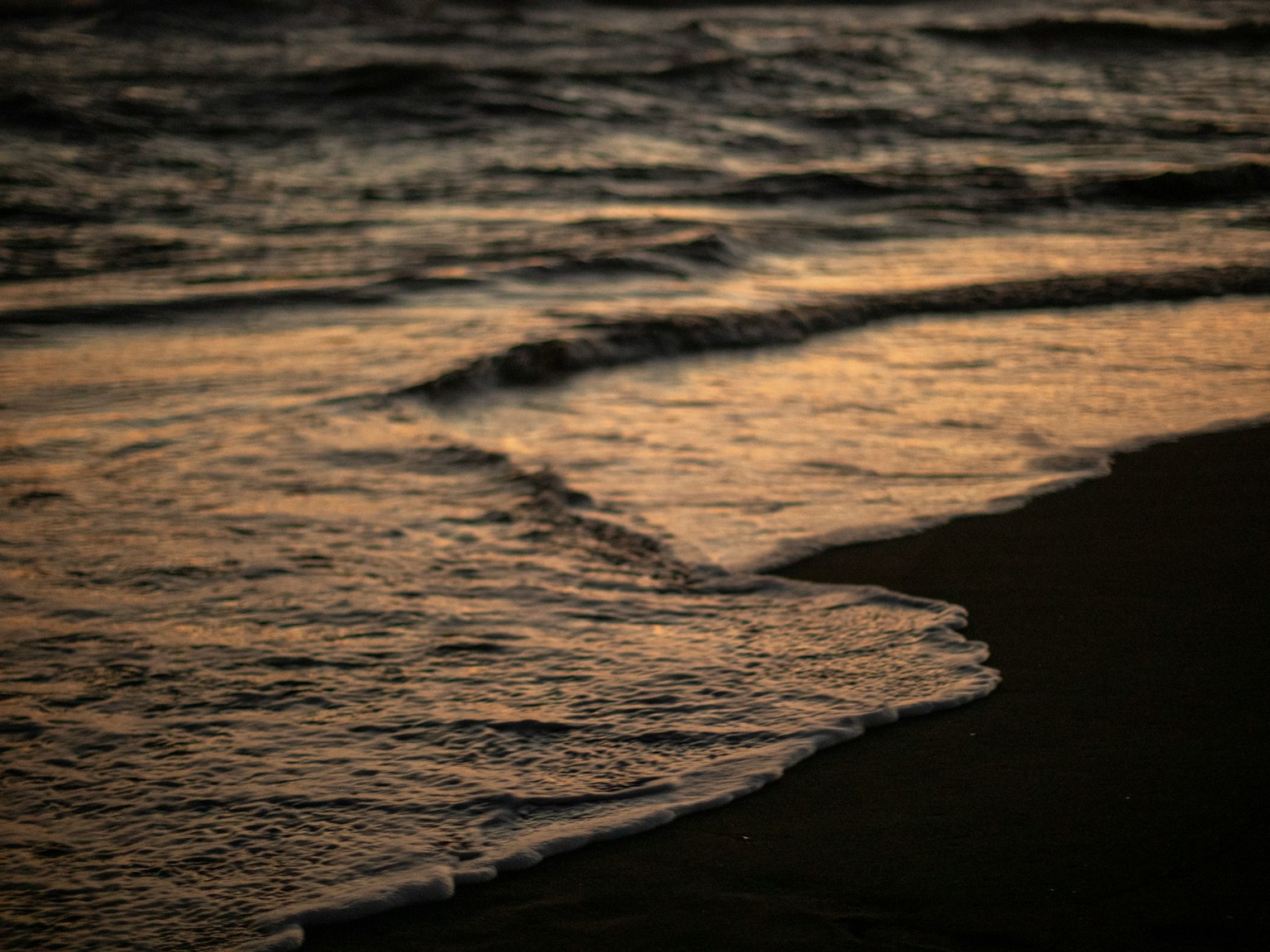 Olas rompiendo en una playa de arena durante el atardecer