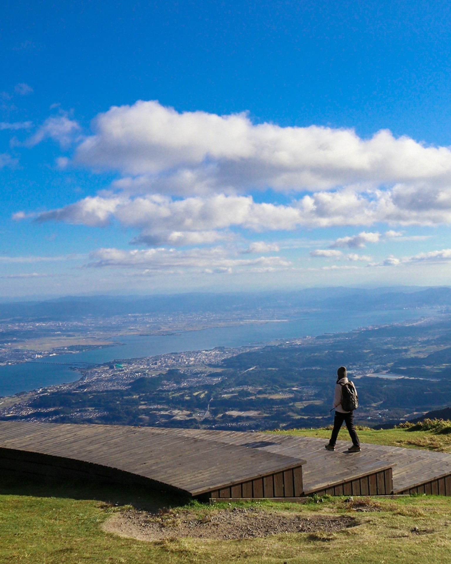 Una persona caminando por un camino de madera con vista a montañas y agua
