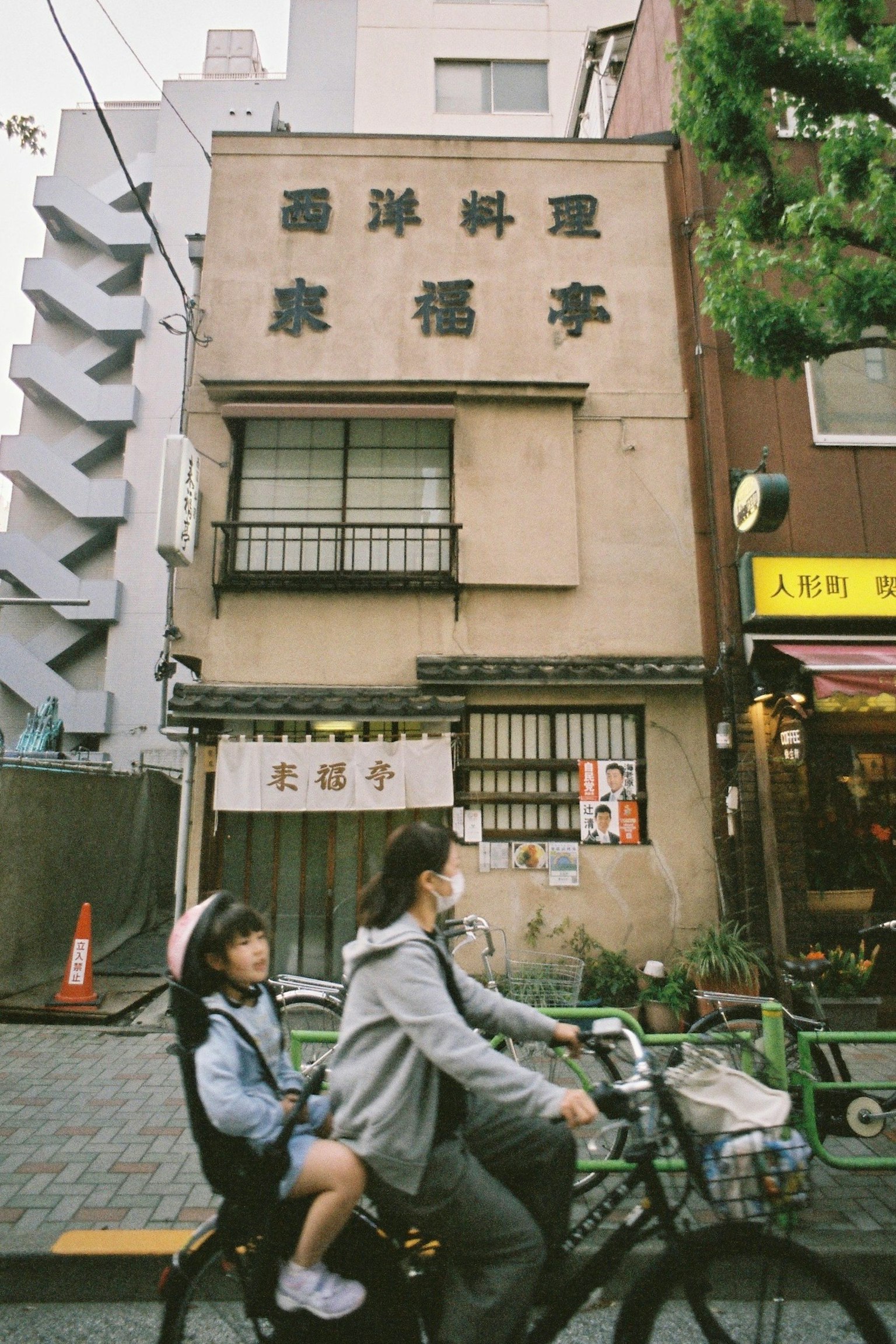 Mère et enfant à vélo devant un ancien restaurant japonais