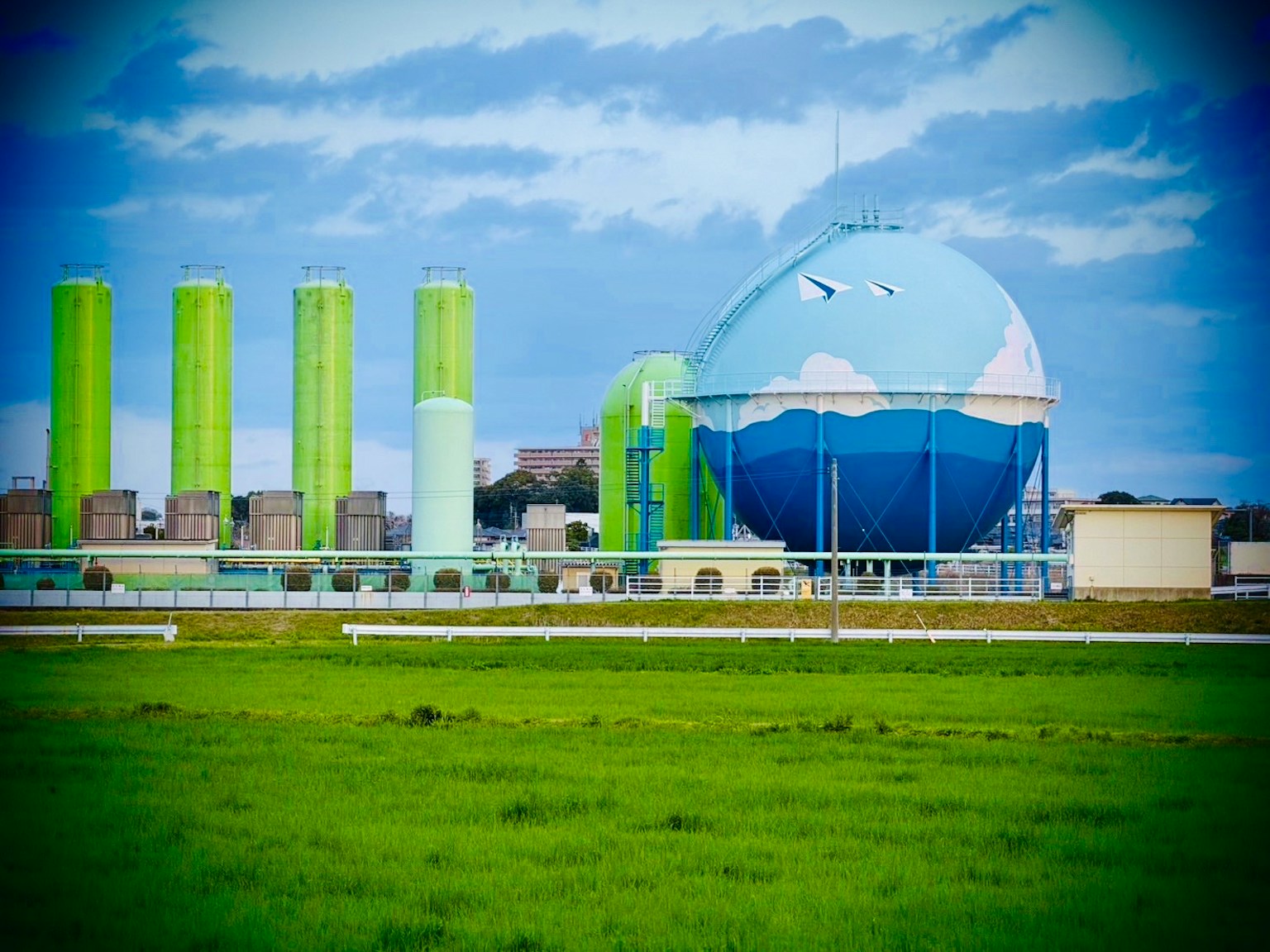 Grand réservoir de gaz avec un design de ciel bleu et de nuages blancs aux côtés de structures cylindriques vertes