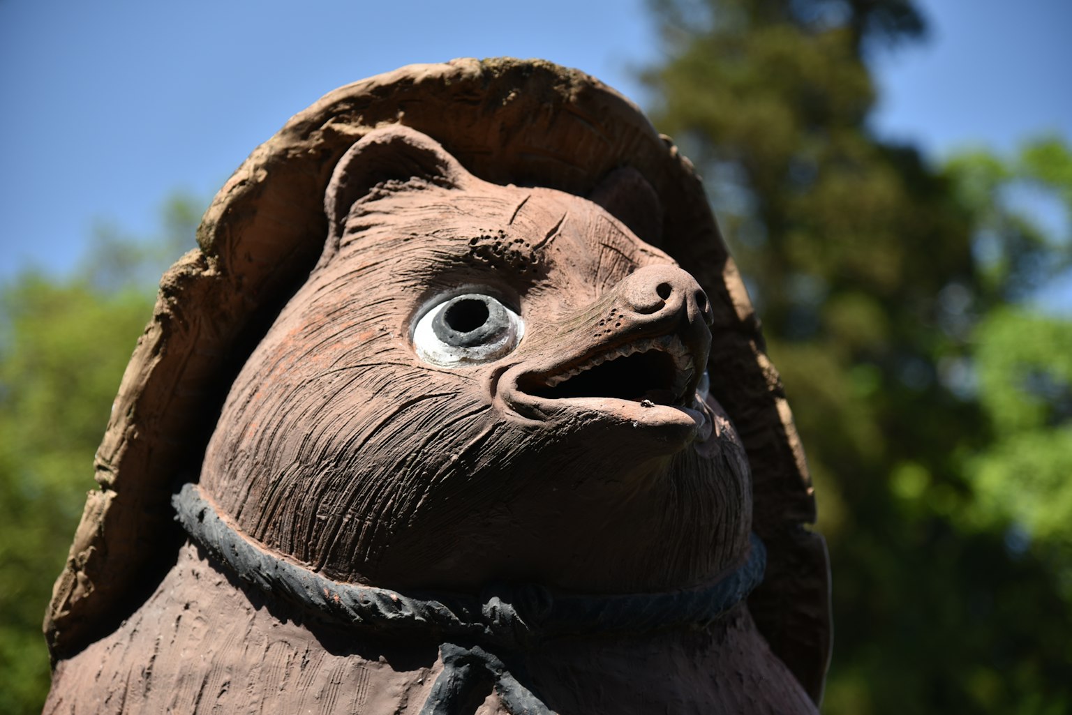 Estatua de arcilla de un tanuki con grandes ojos y una expresión sorprendida que lleva un sombrero tradicional