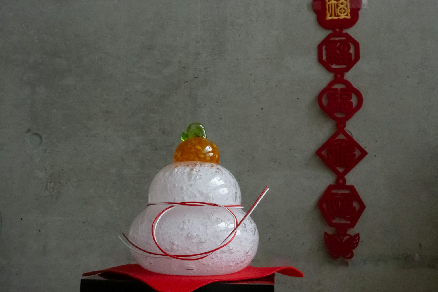 Un objeto decorativo en forma de muñeco de nieve con una parte superior naranja y cinta roja sobre una tela roja