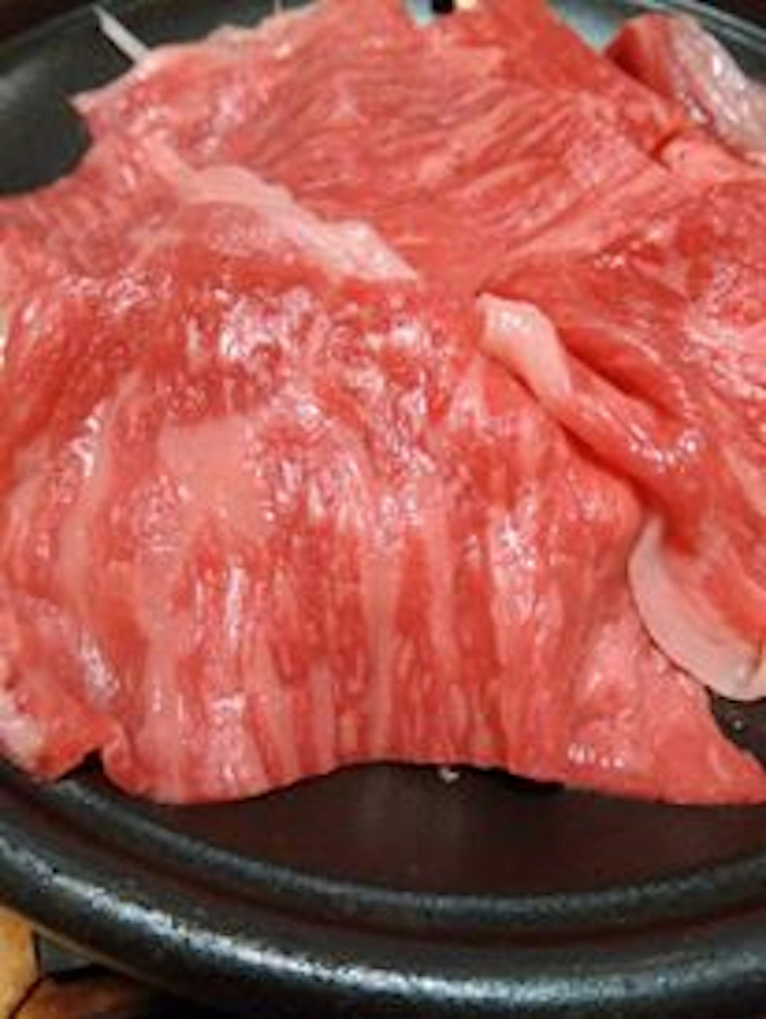 Daging Wagyu yang diiris tipis disusun di atas piring hitam