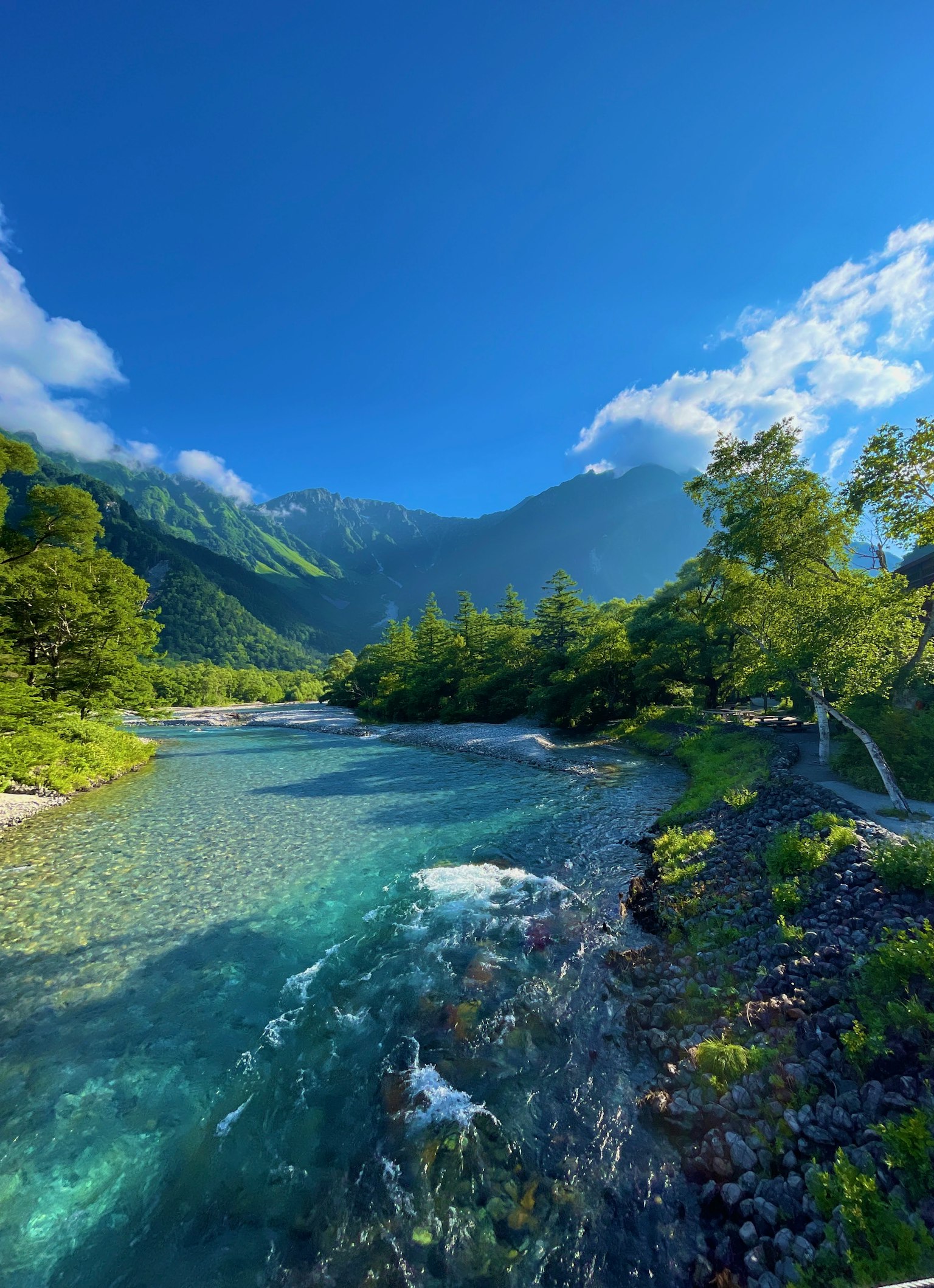 Malersicher Blick auf einen klaren Fluss umgeben von üppigem Grün und Bergen unter einem blauen Himmel