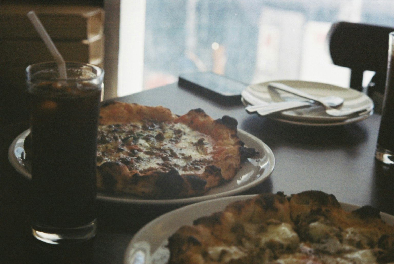 Due pizze su un tavolo con una bevanda e posate
