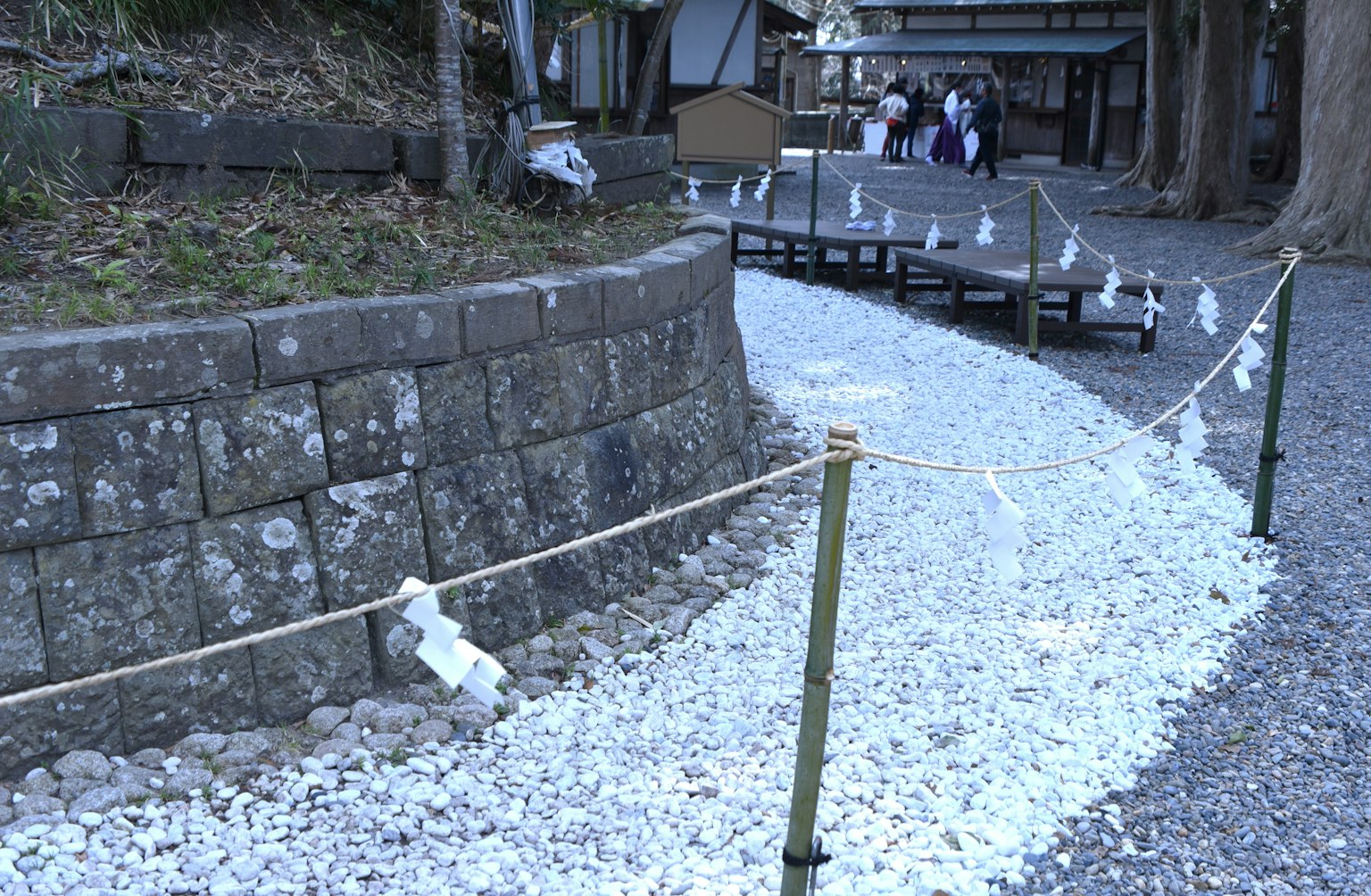 A winding path of white pebbles with a stone wall and traditional buildings in the background