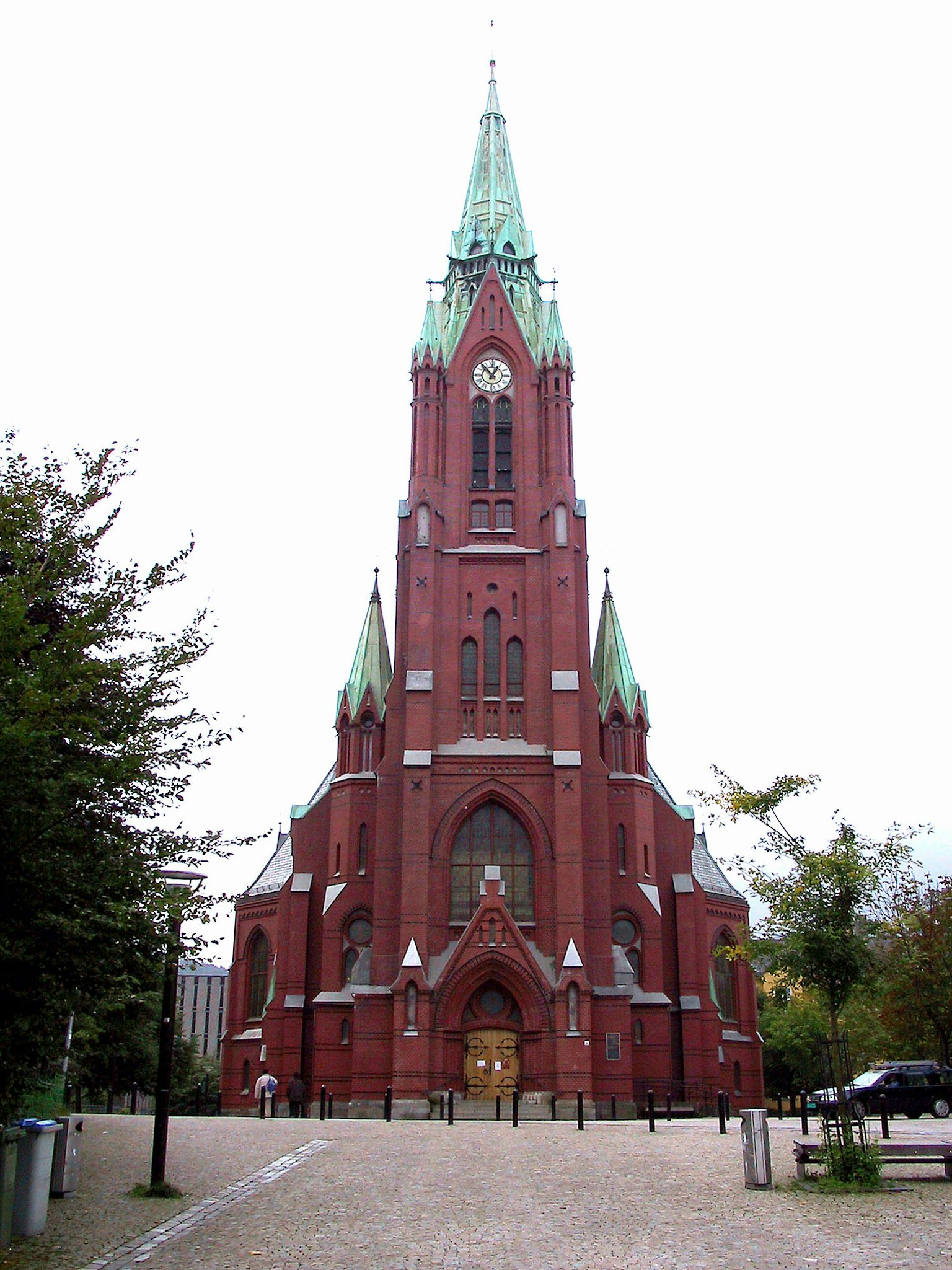 Äußeres einer roten Backsteinkirche mit hohen Türmen und grünen Dächern