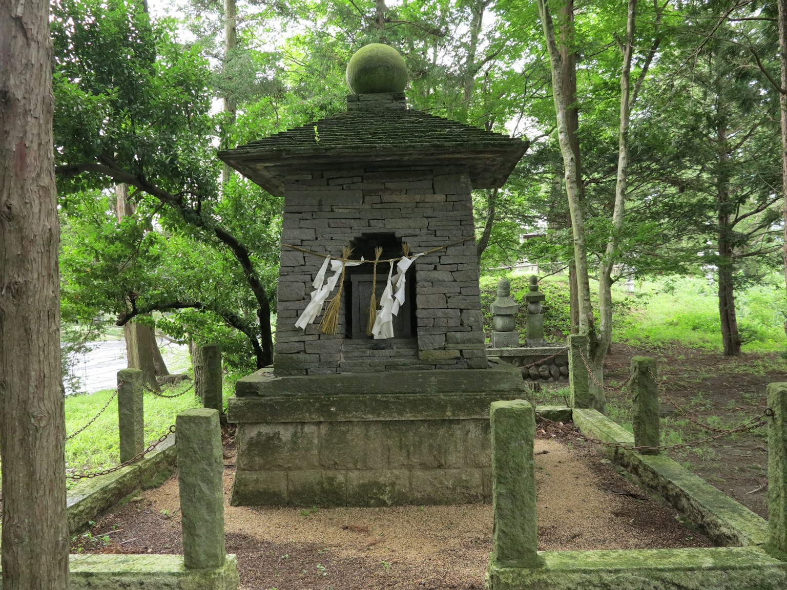 Monument en pierre entouré de verdure luxuriante avec une décoration sphérique sur le dessus