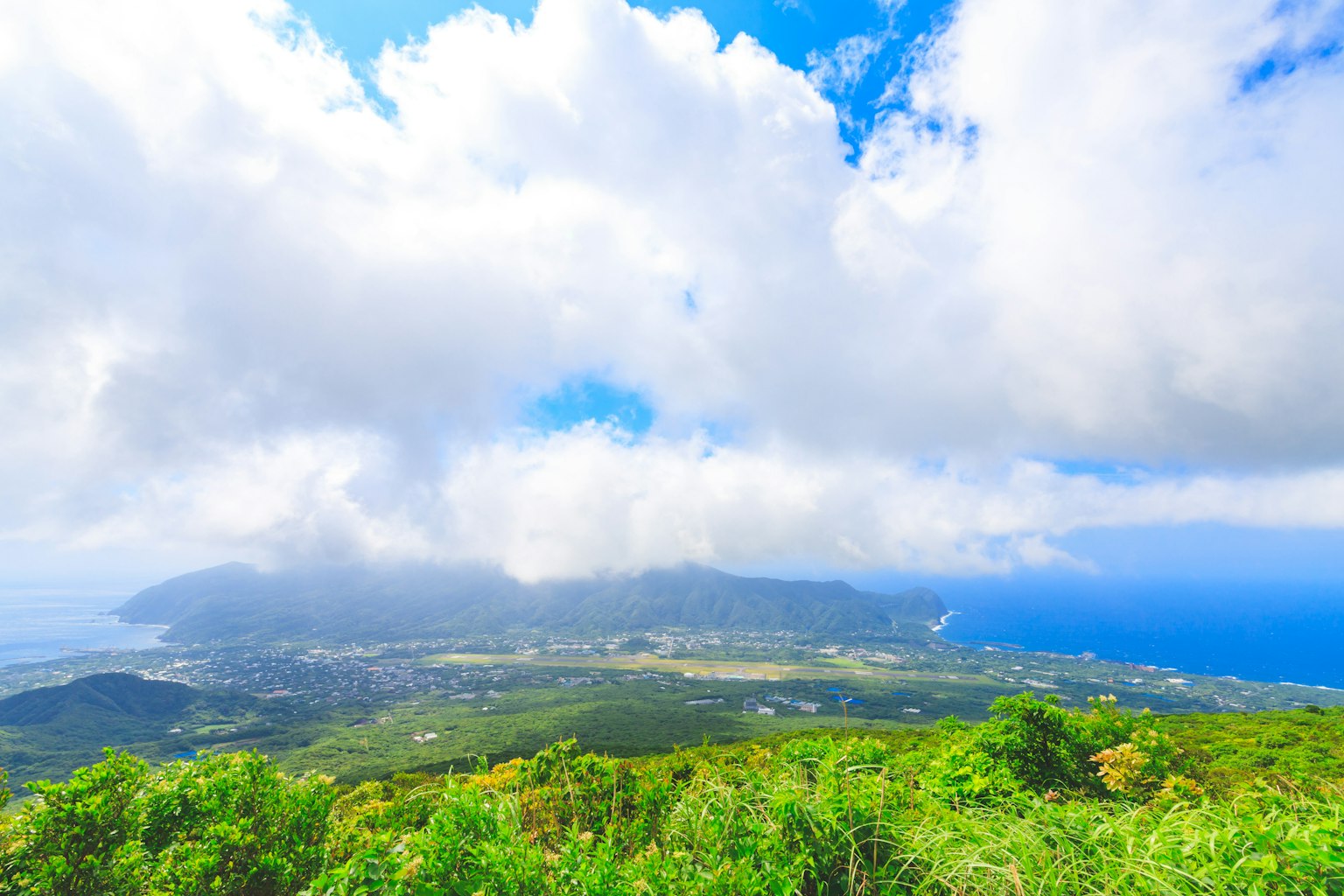Lush green hillside with a view of the ocean and a cloudy sky