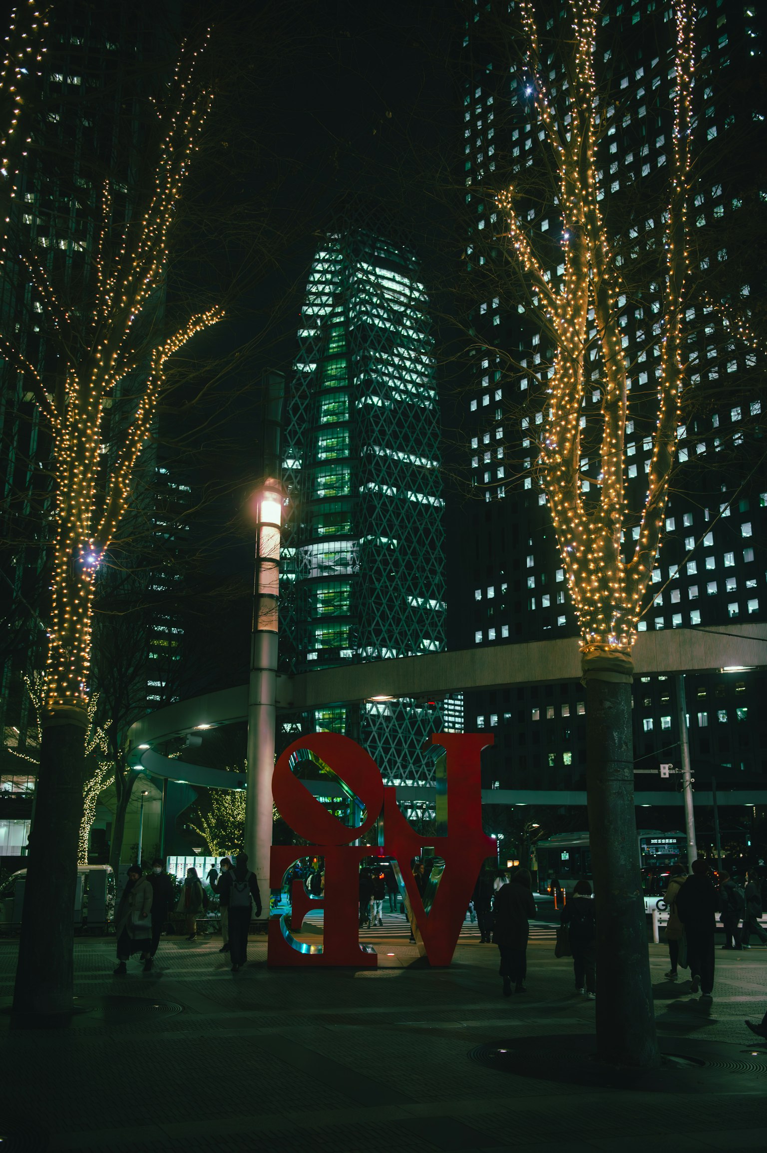 Paesaggio urbano notturno con alberi illuminati e una grande scultura rossa