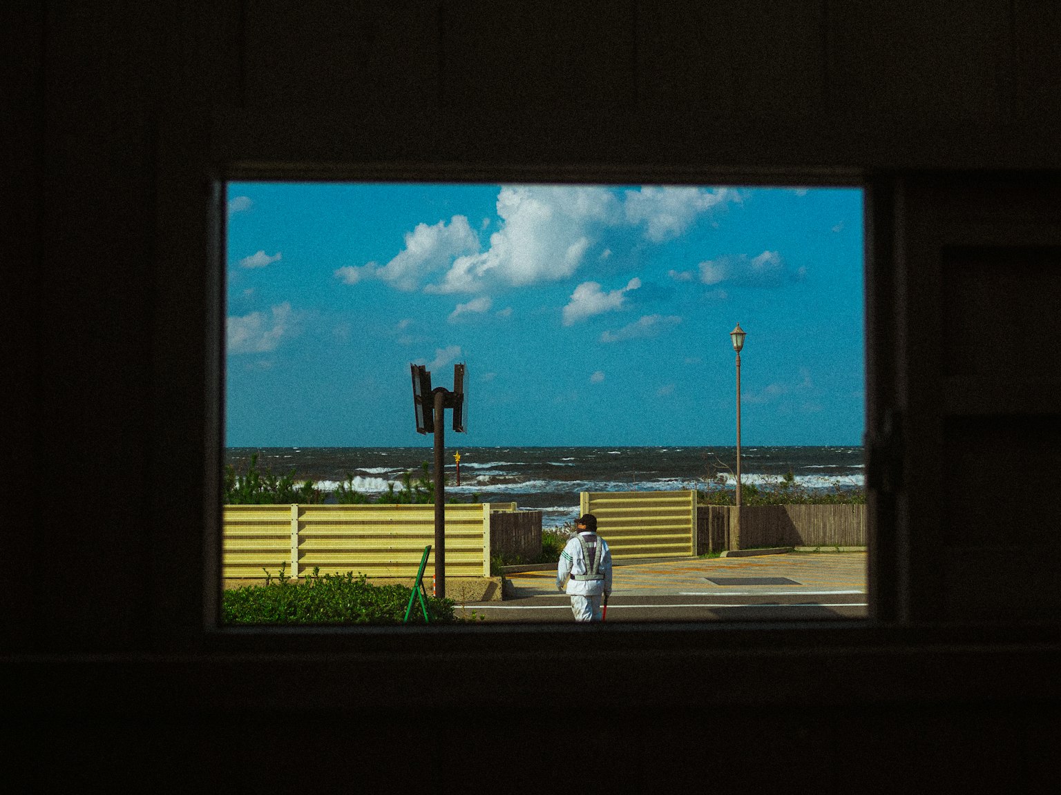 窓から見える青い空と白い雲の下を歩く人物と海の景色