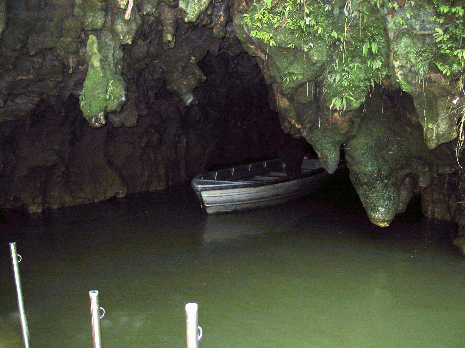 Una scena serena con una piccola barca che galleggia su acqua ferma all'interno di una caverna circondata da rocce coperte di muschio