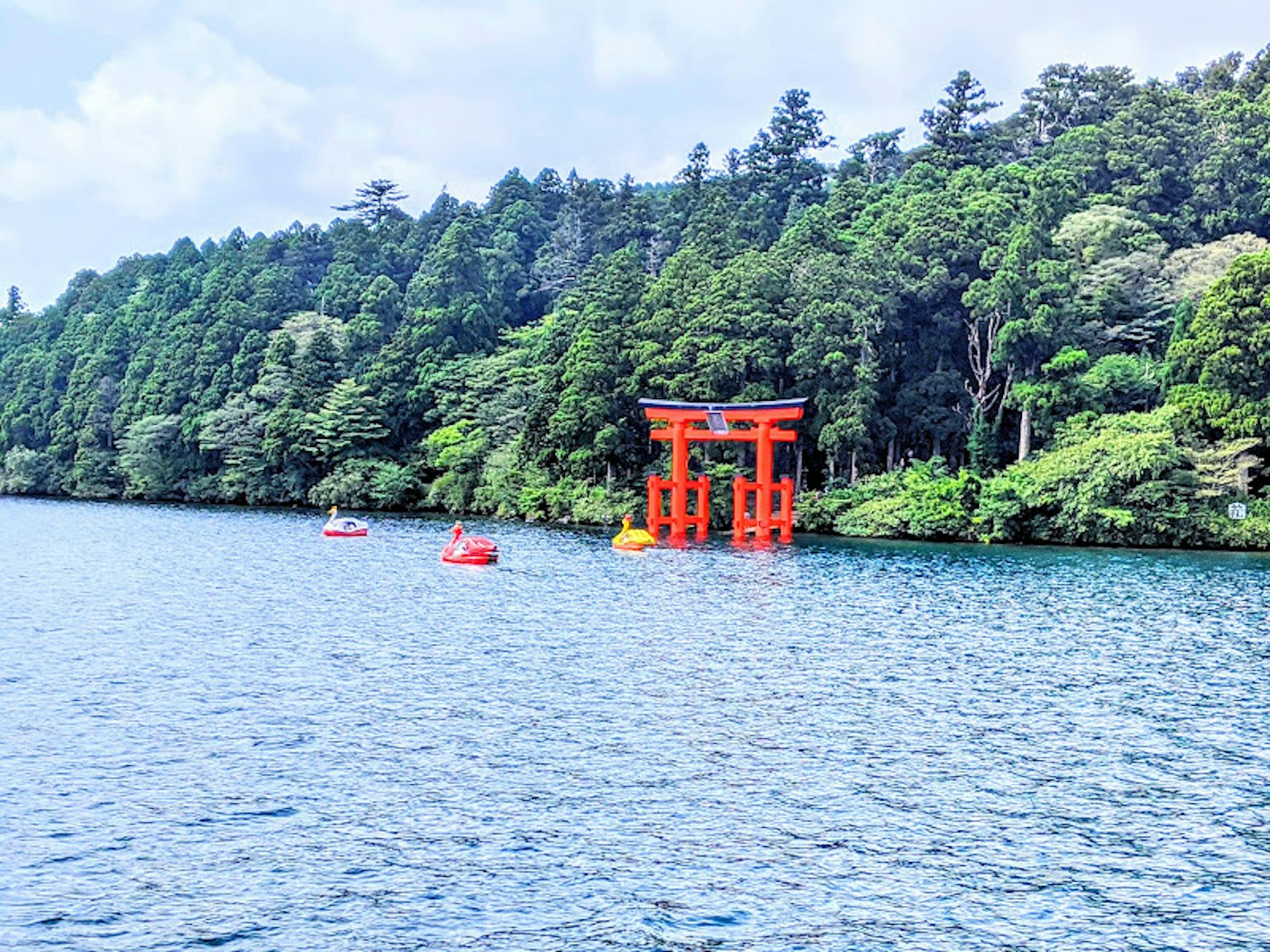 Malersicher Blick auf ein rotes Torii am Ufer eines Sees umgeben von üppigem Grün