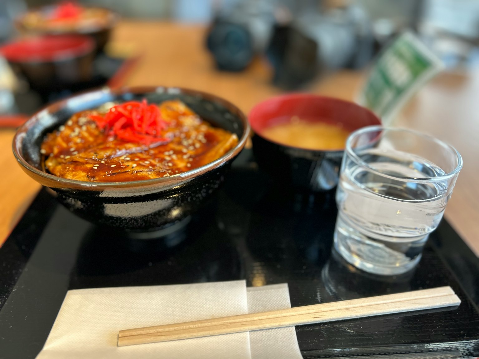 테이블에 놓인 일본 식사 세트 닭고기 가츠동에 절인 생강이 얹혀 있다 미소국과 물이 담긴 유리잔이 포함되어 있다
