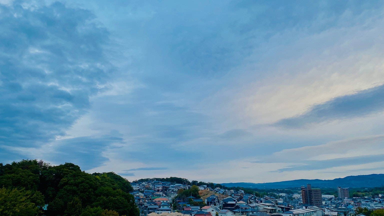 Eine Panoramaansicht mit blauem Himmel und Wolken sowie einer Stadtlandschaft, die von üppigem Grün umgeben ist