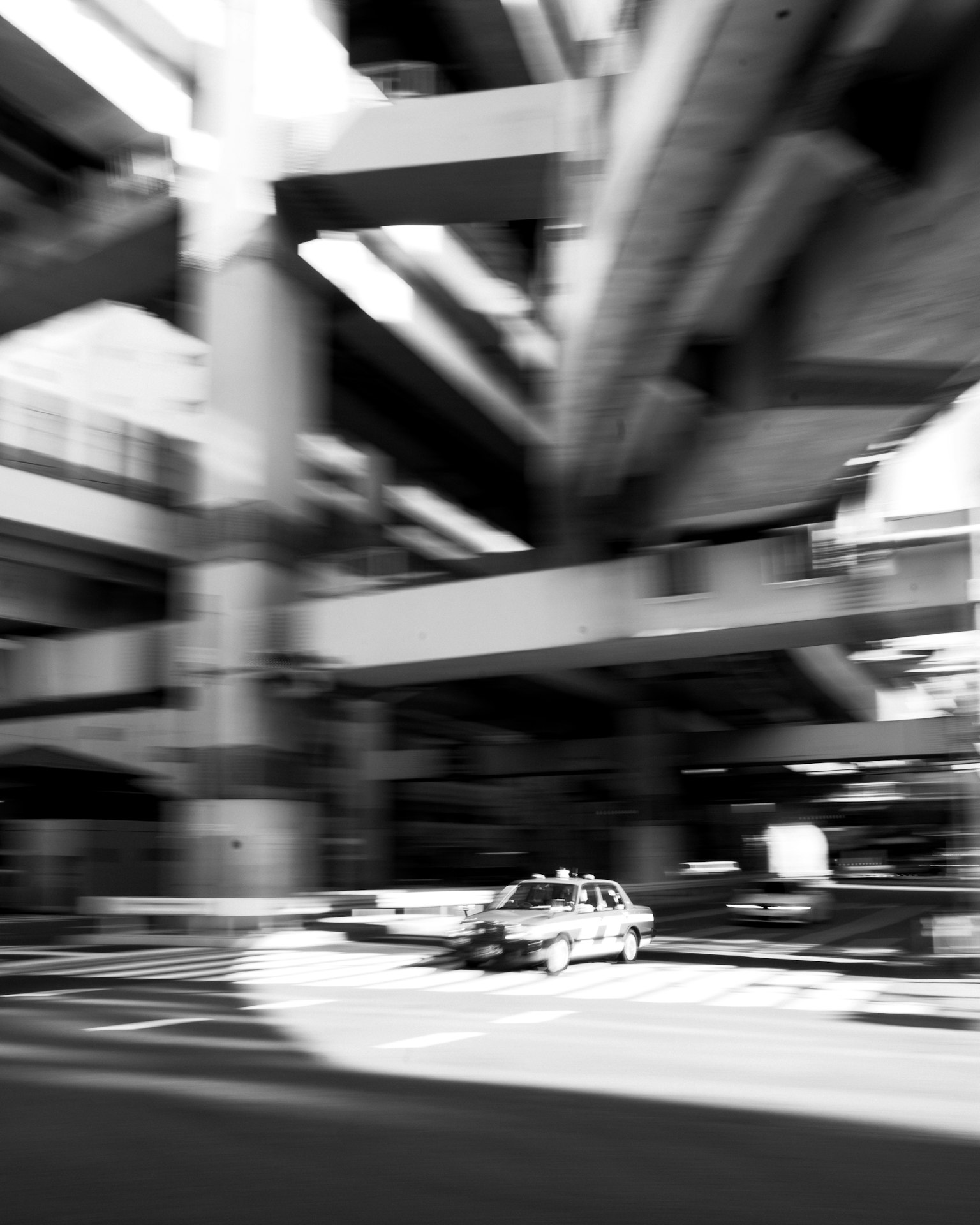 Scena urbana in bianco e nero con complessi sovrappassi e un'auto che passa sotto