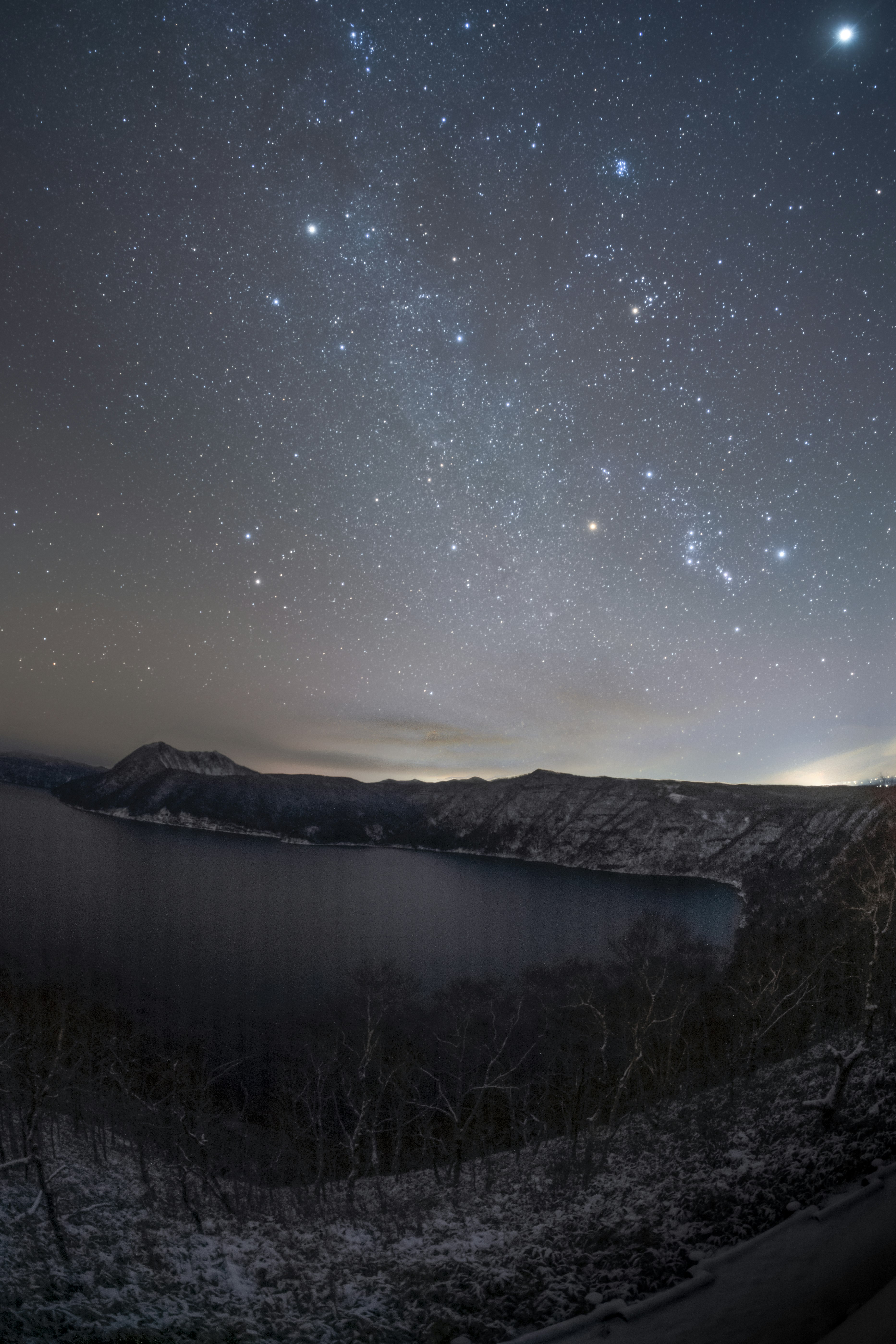 vista nocturna de crestas montañosas y un lago bajo un cielo estrellado