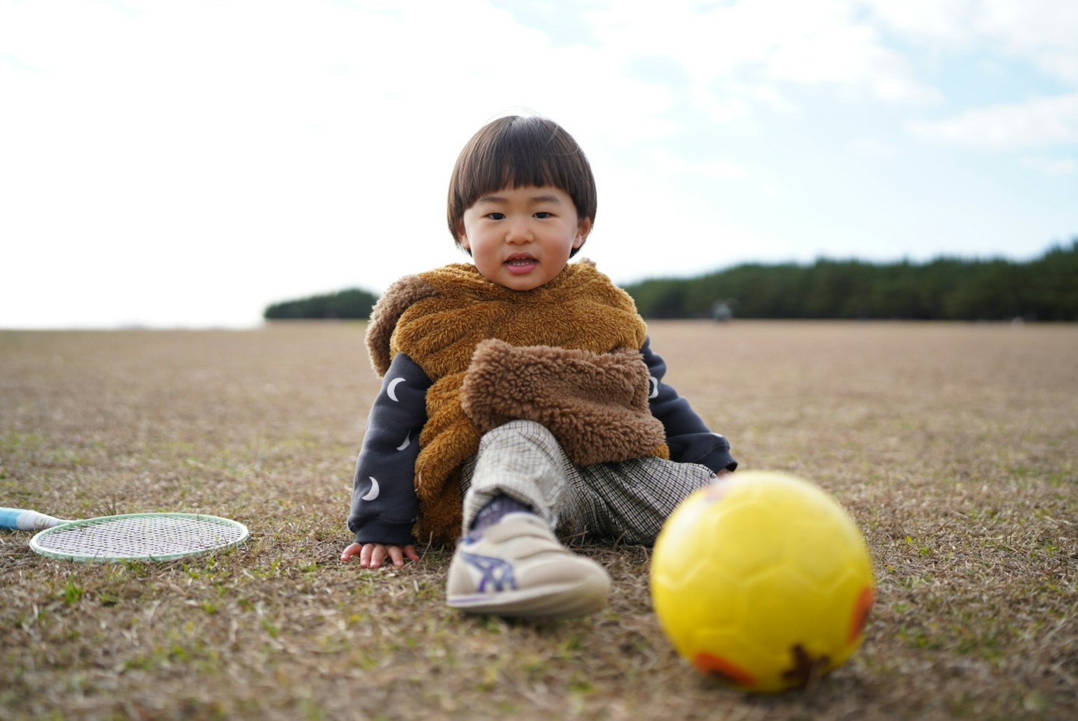 Anak duduk di rumput di samping bola sepak kuning