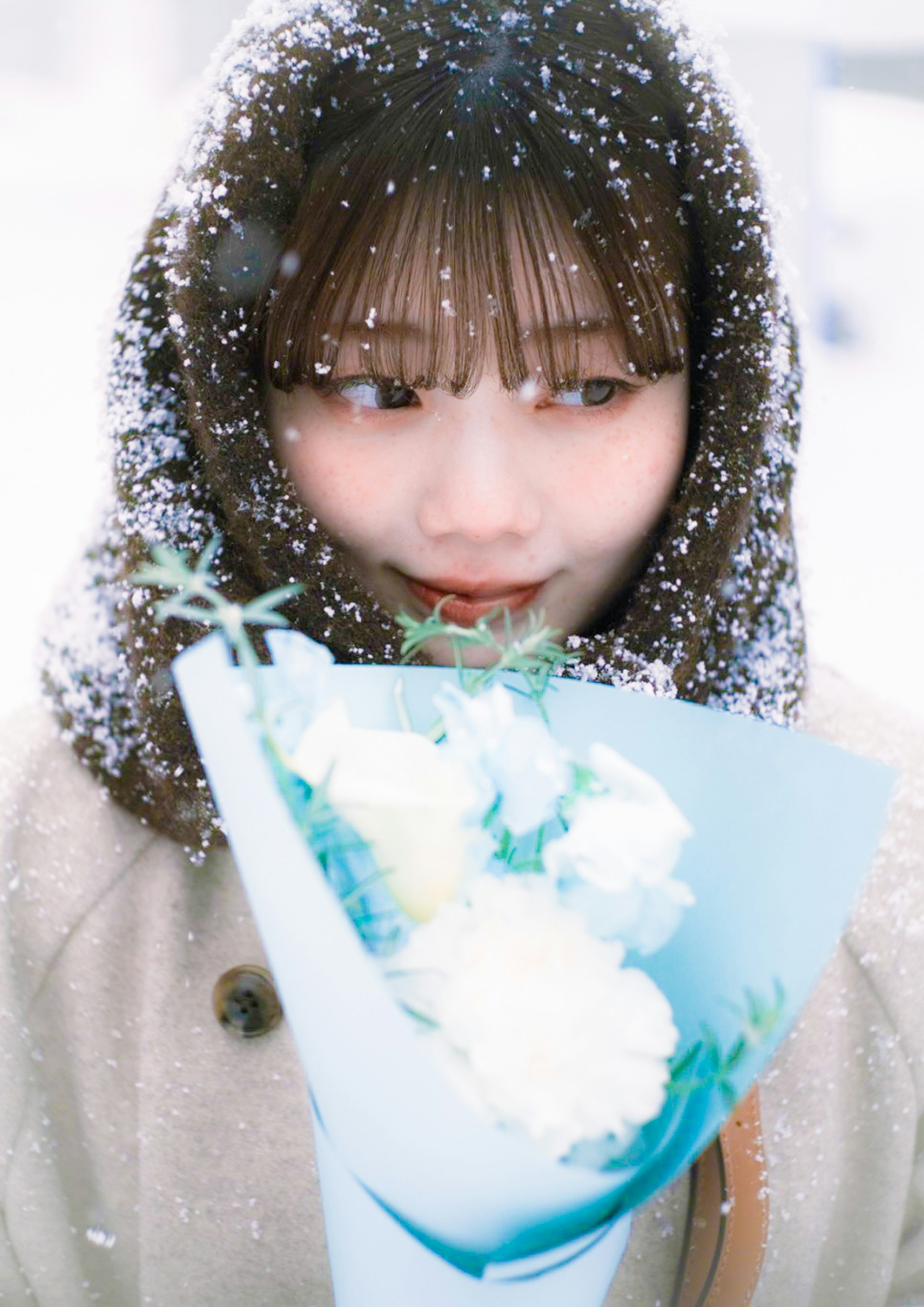 雪の舞うフード付きコートの子が花束を抱える