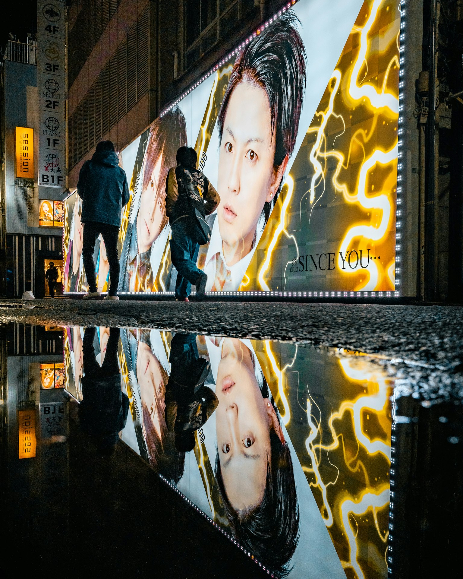 Large advertisement billboard with reflections in a wet street at night