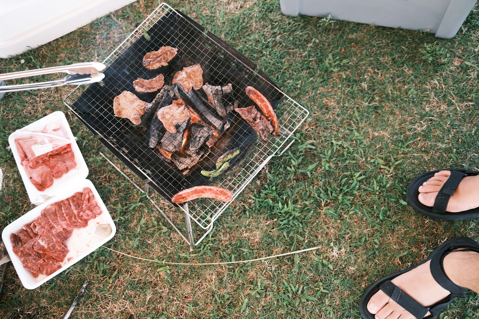 Viande grillée sur un barbecue avec des pieds en sandales à proximité