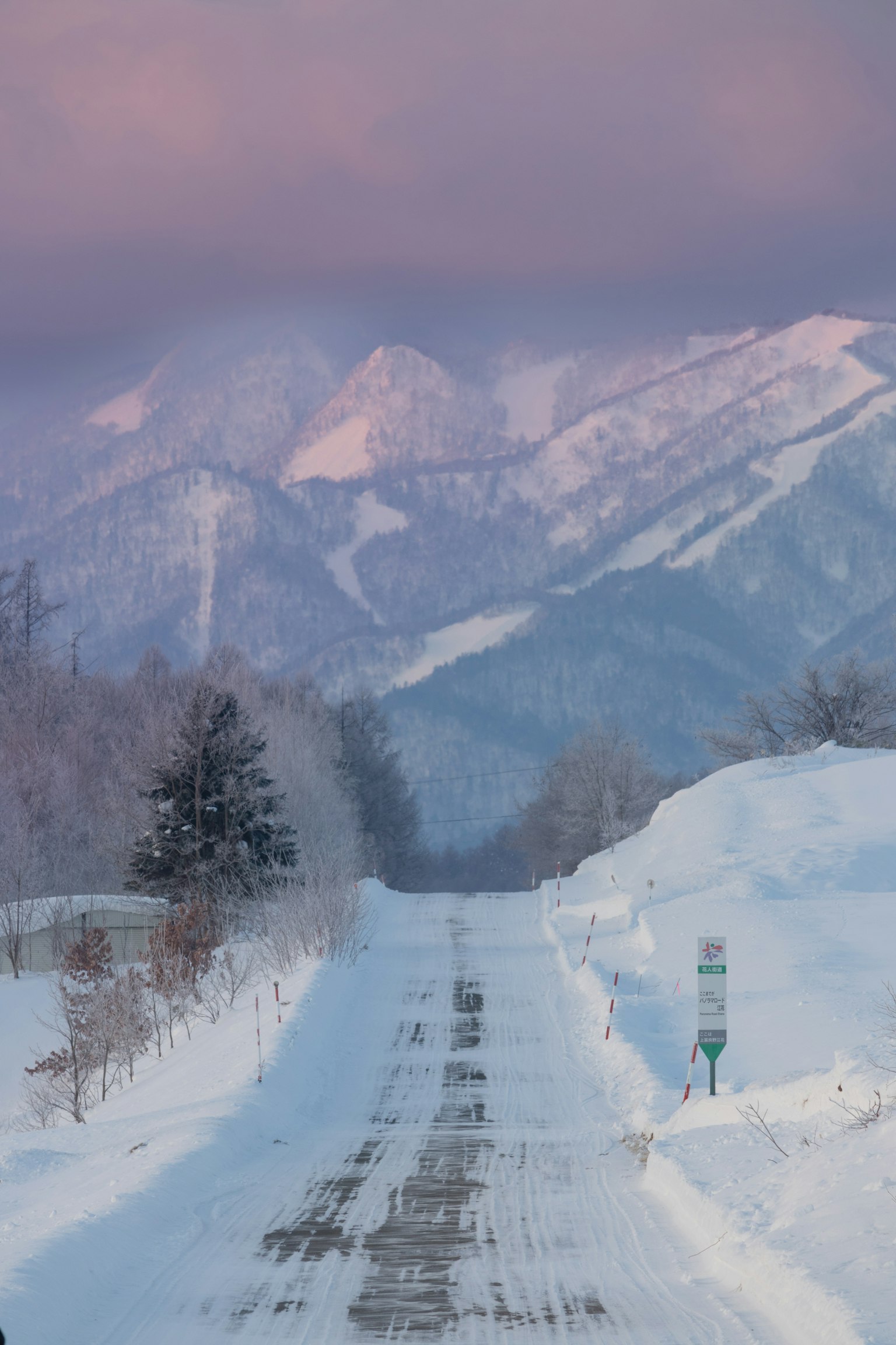 Schneebedeckte Straße, die zu fernen Bergen unter einem pastellfarbenen Himmel führt