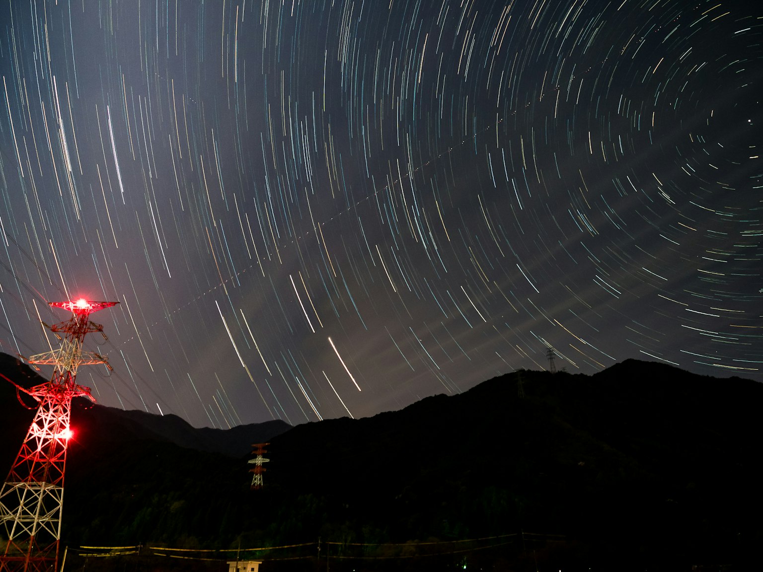 Traînées d'étoiles dans le ciel nocturne avec une tour de transmission éclairée en rouge