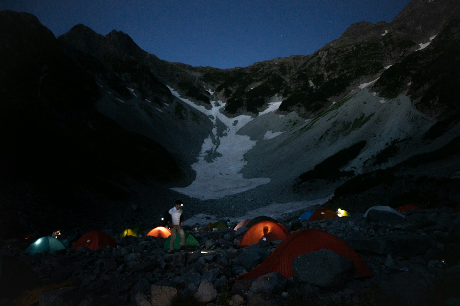 Tenda berwarna-warni yang dipasang di perkemahan gunung di bawah langit malam dengan gletser yang terlihat
