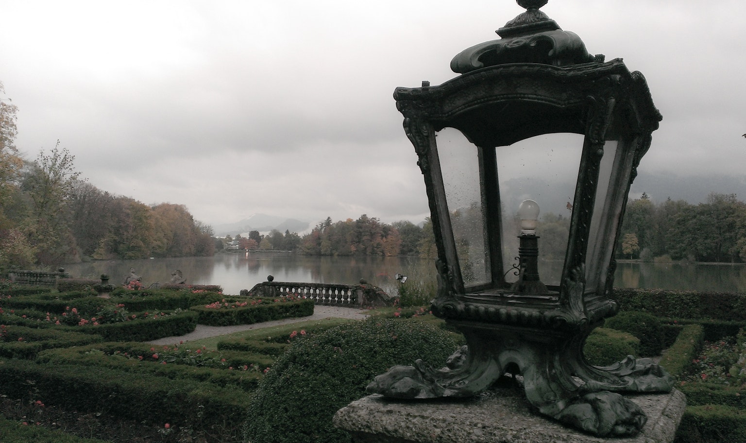 An old lantern near a misty lake with a well-manicured garden