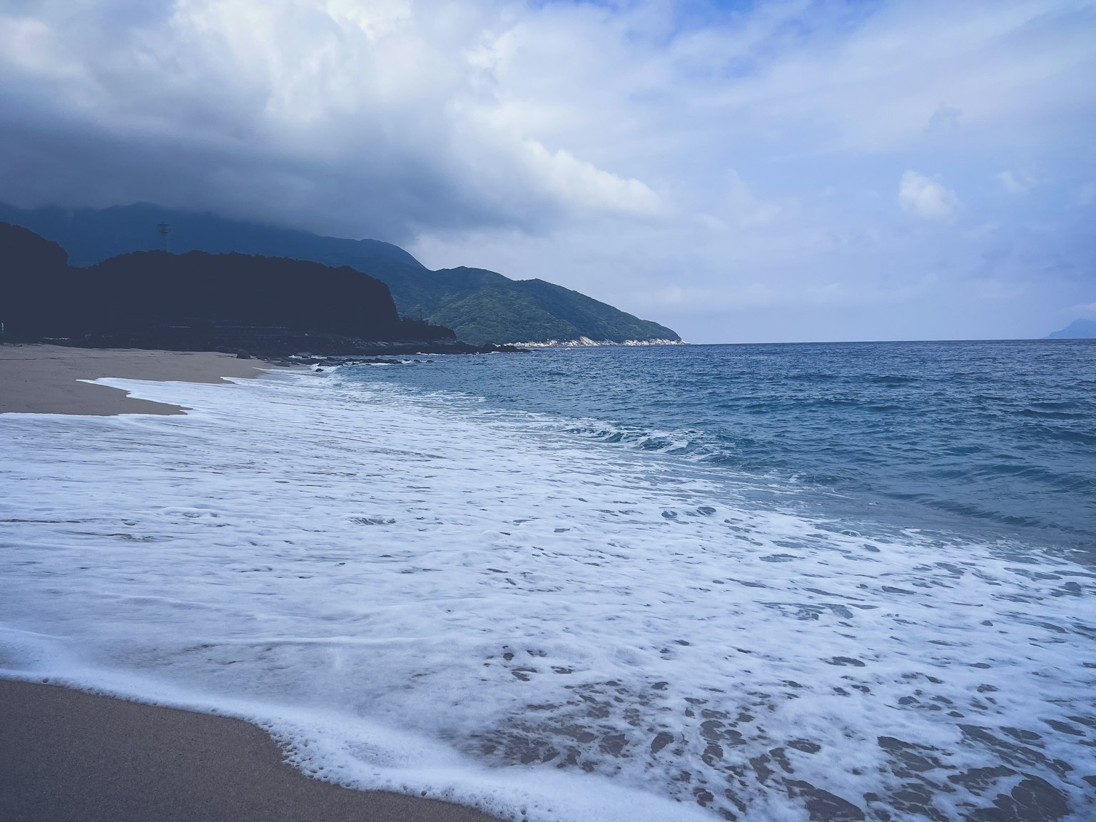 Vue panoramique des vagues de l'océan s'écrasant sur une plage de sable avec des montagnes en arrière-plan