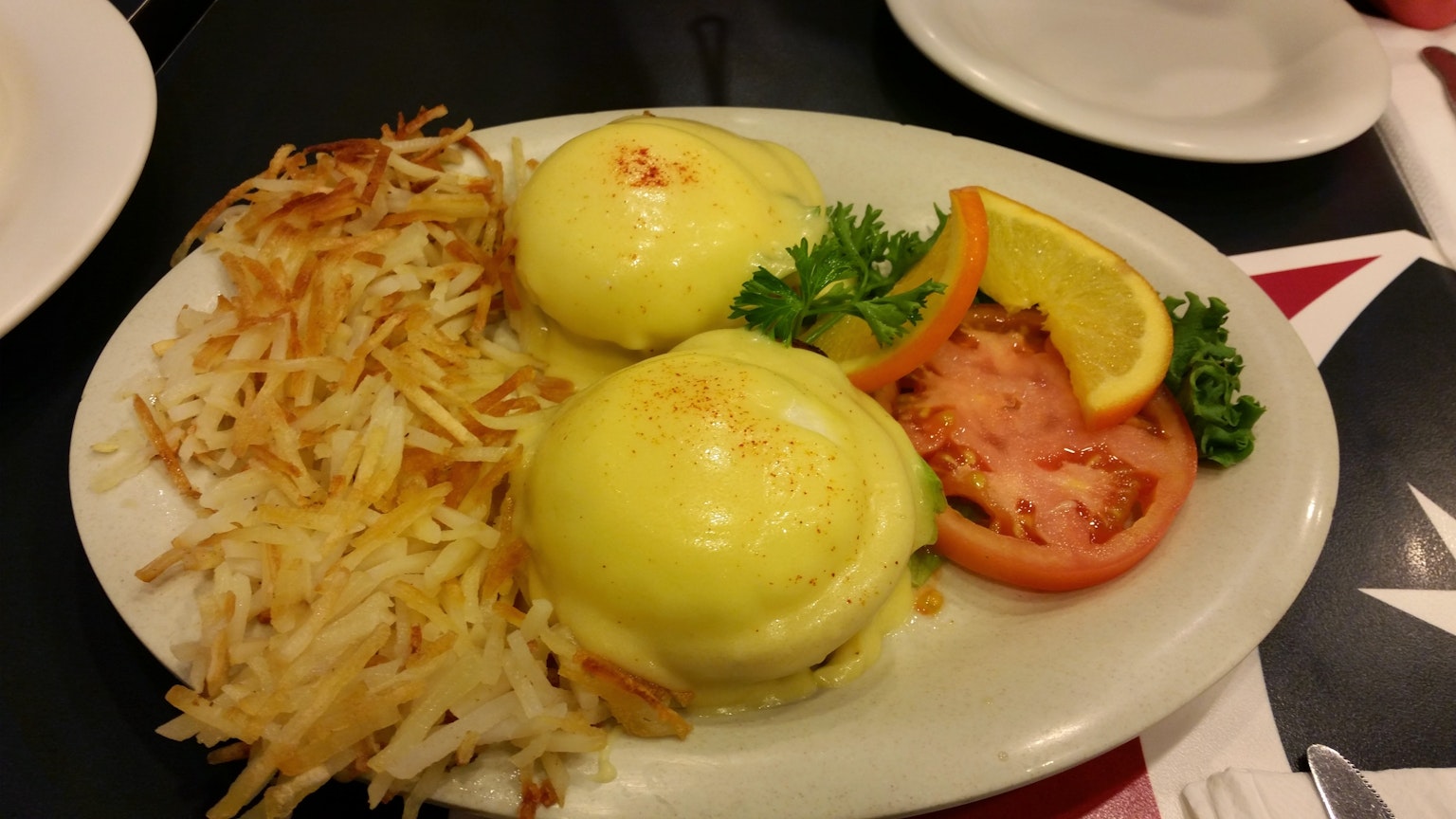 Teller mit Eggs Benedict und Röstkartoffeln frischer Tomate und Orangenscheiben