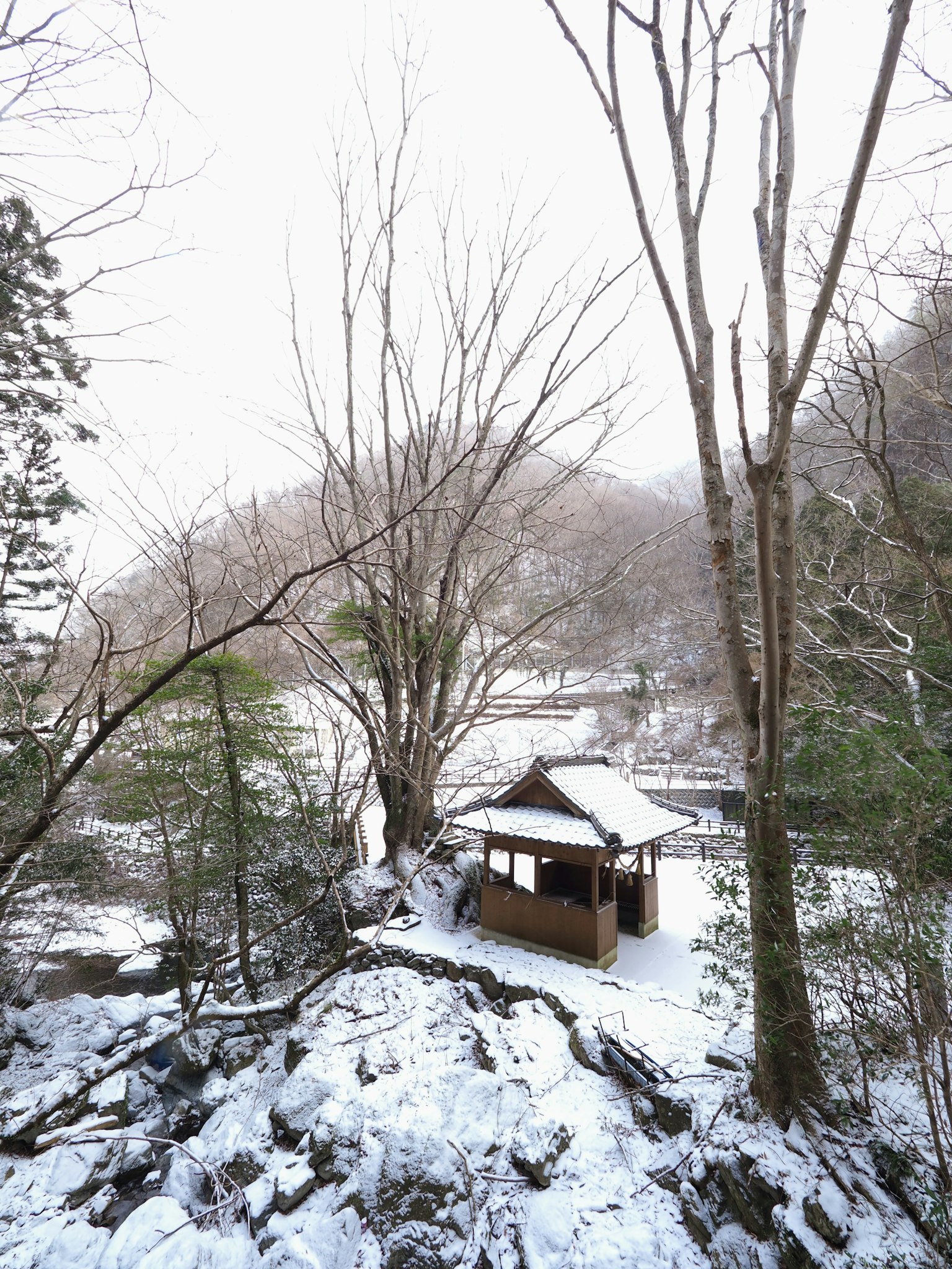 Schneebedecktes Häuschen in einer bergigen Landschaft mit kahlen Bäumen