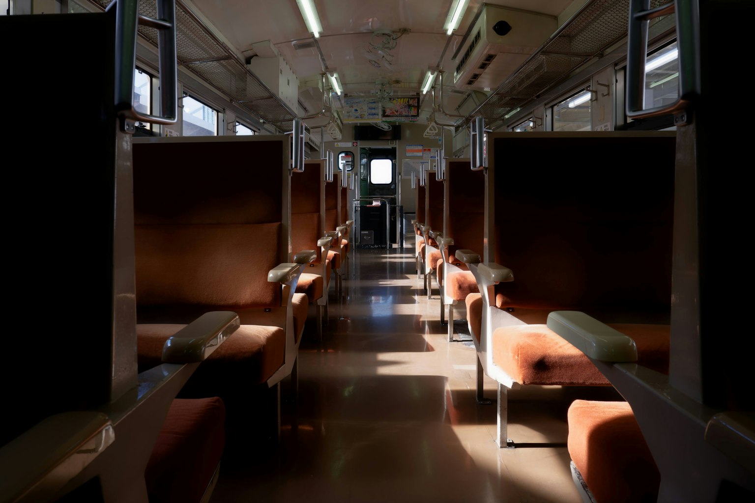 Interior of an empty train carriage with bright lighting and brown seats
