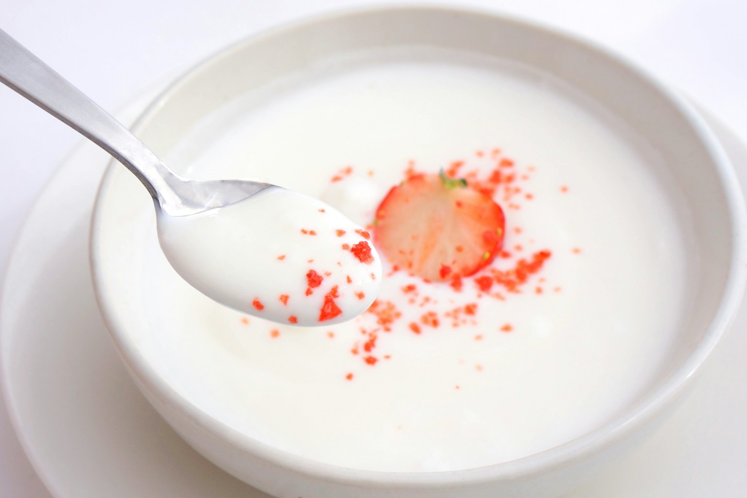 Dessert cremoso in una ciotola bianca con una fetta di fragola e decorazioni rosse