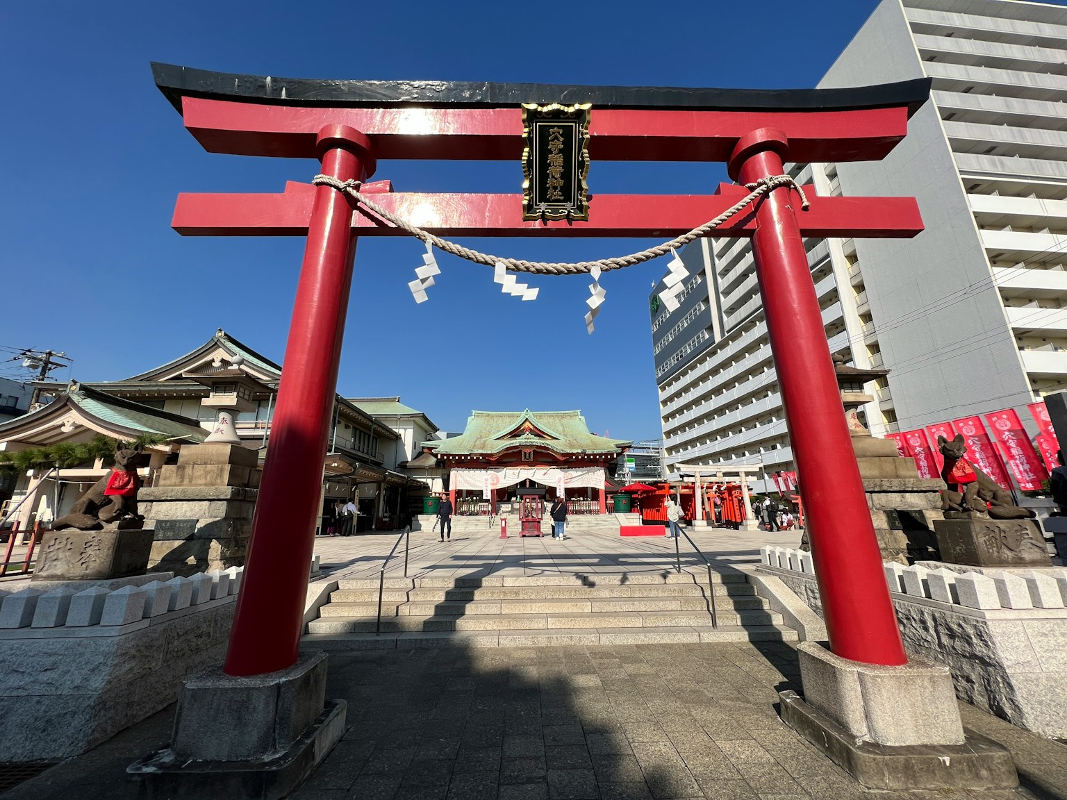 Gerbang torii merah tradisional dengan kuil dan bangunan modern di dekatnya