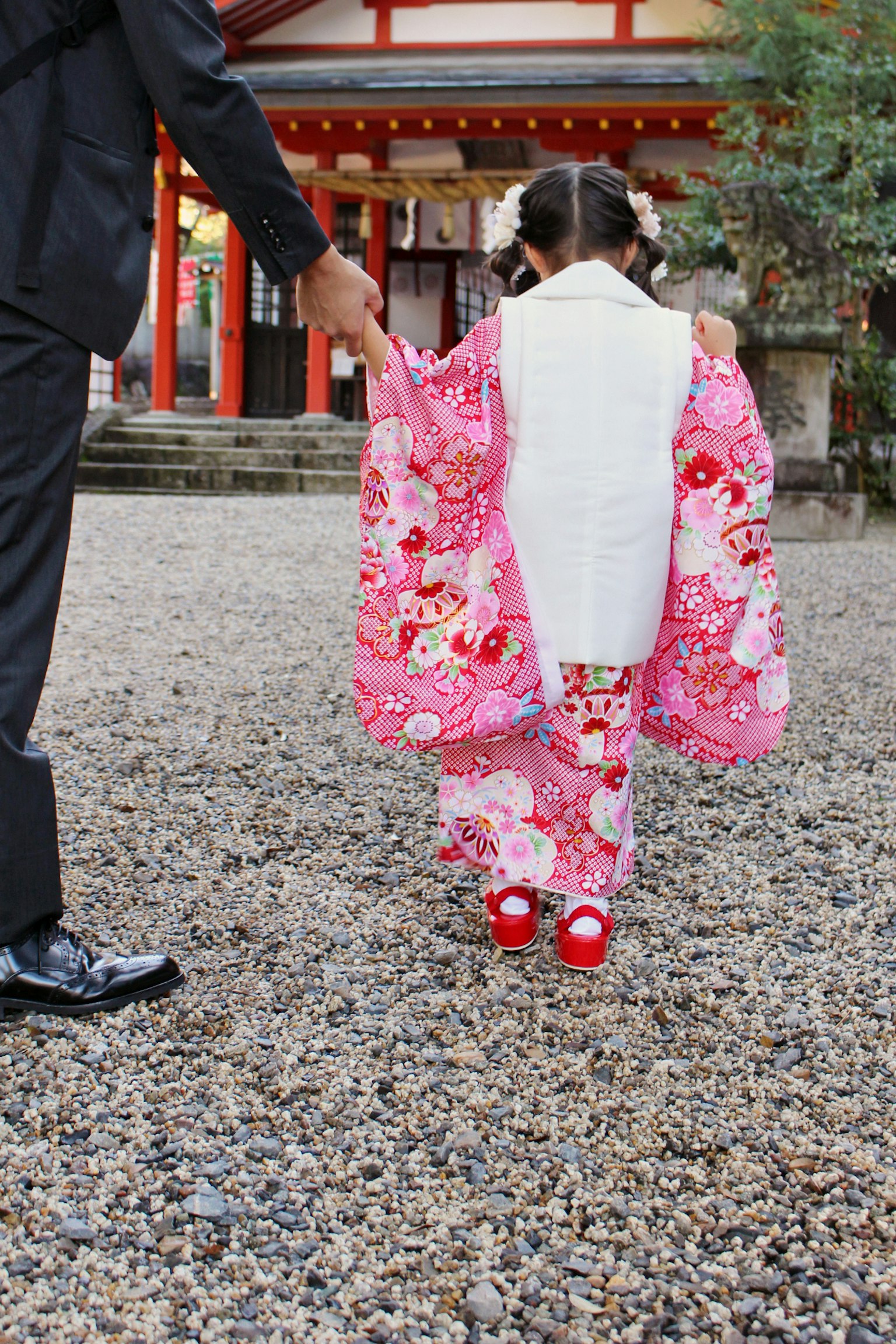 A small girl in a vibrant pink kimono being guided by an adult's hand